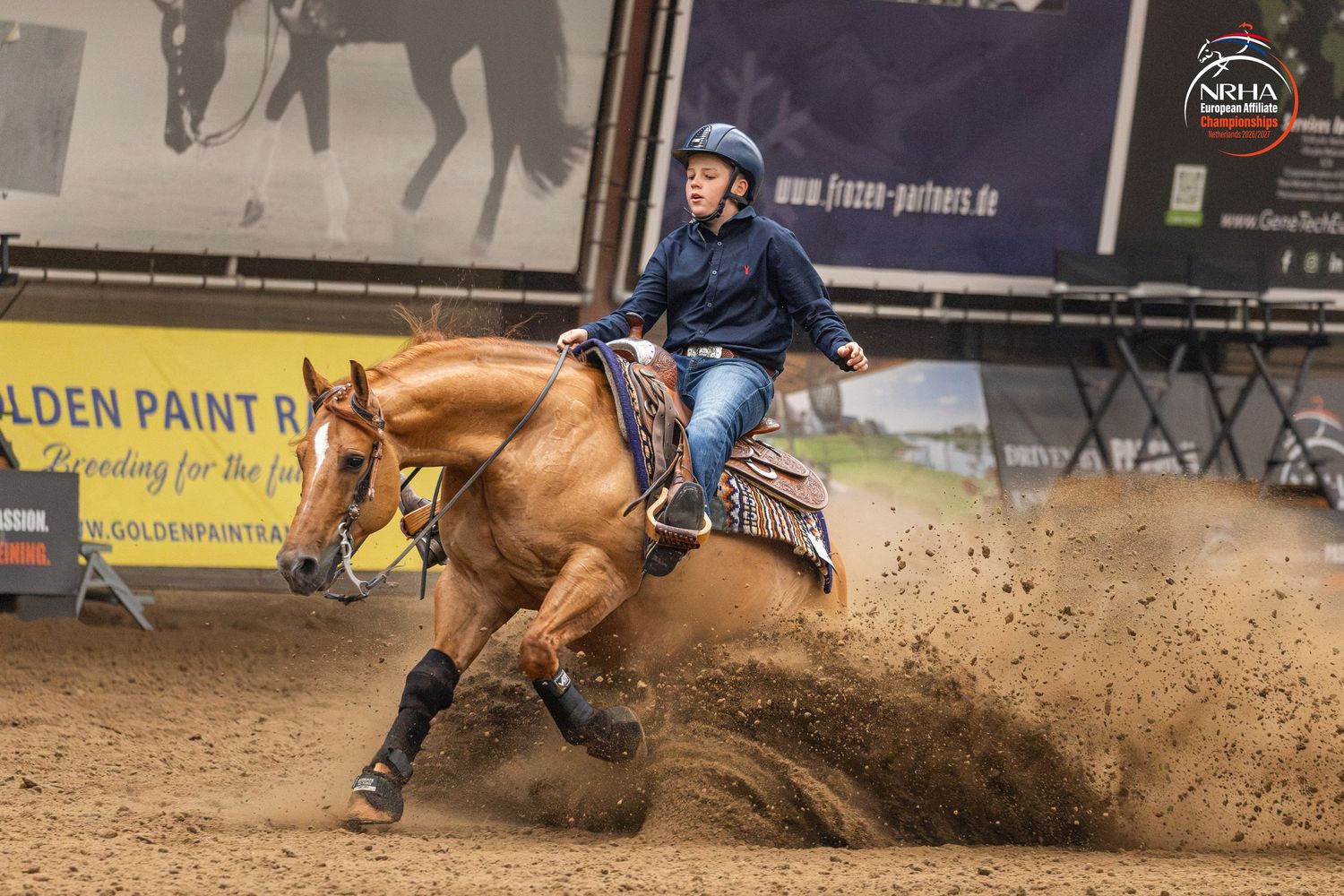 Rider on palomino horse performing sliding stop in Western reining competition on dirt arena.