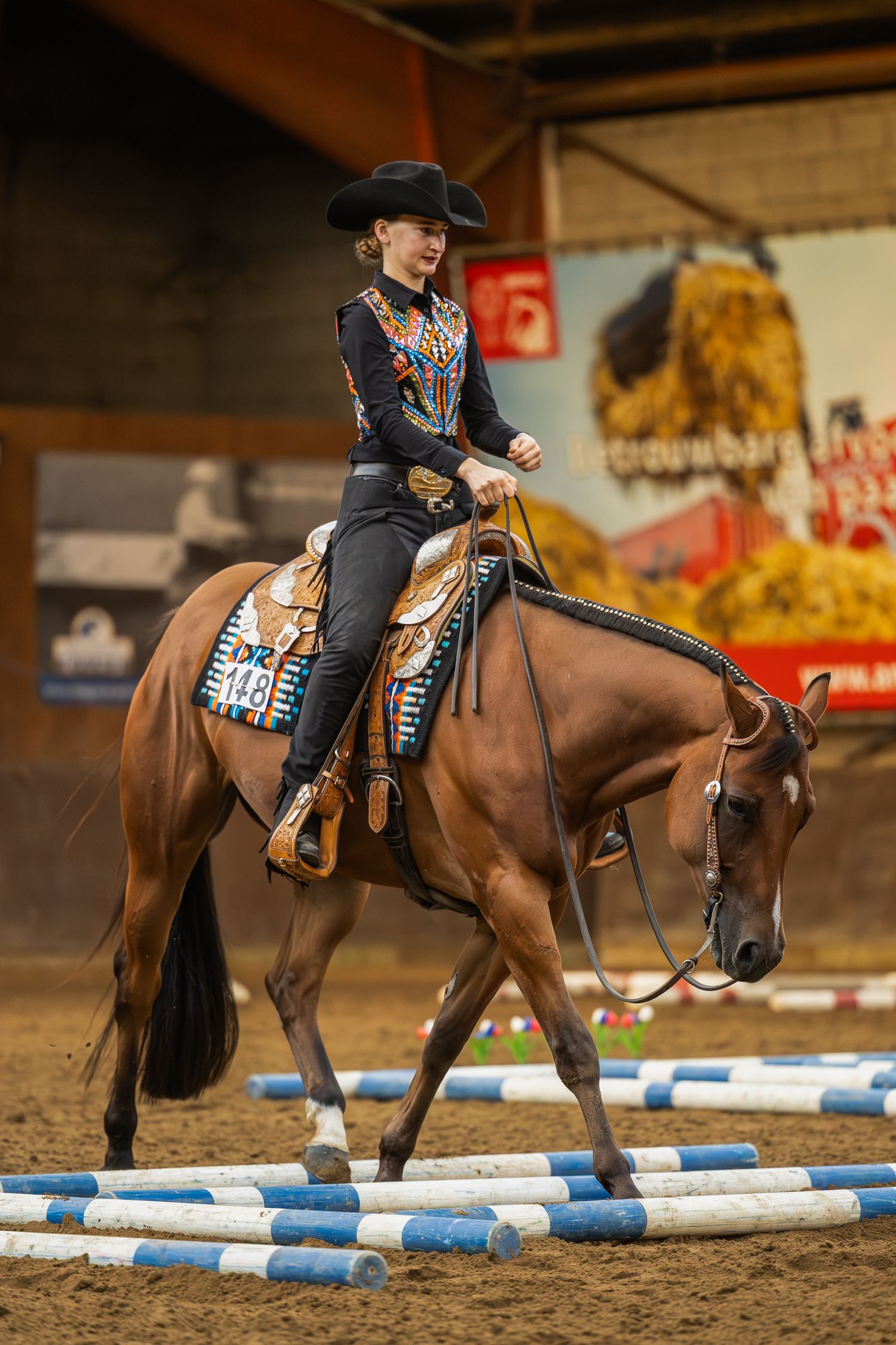 Western rider in black attire navigating horse through poles course in indoor arena competition.
