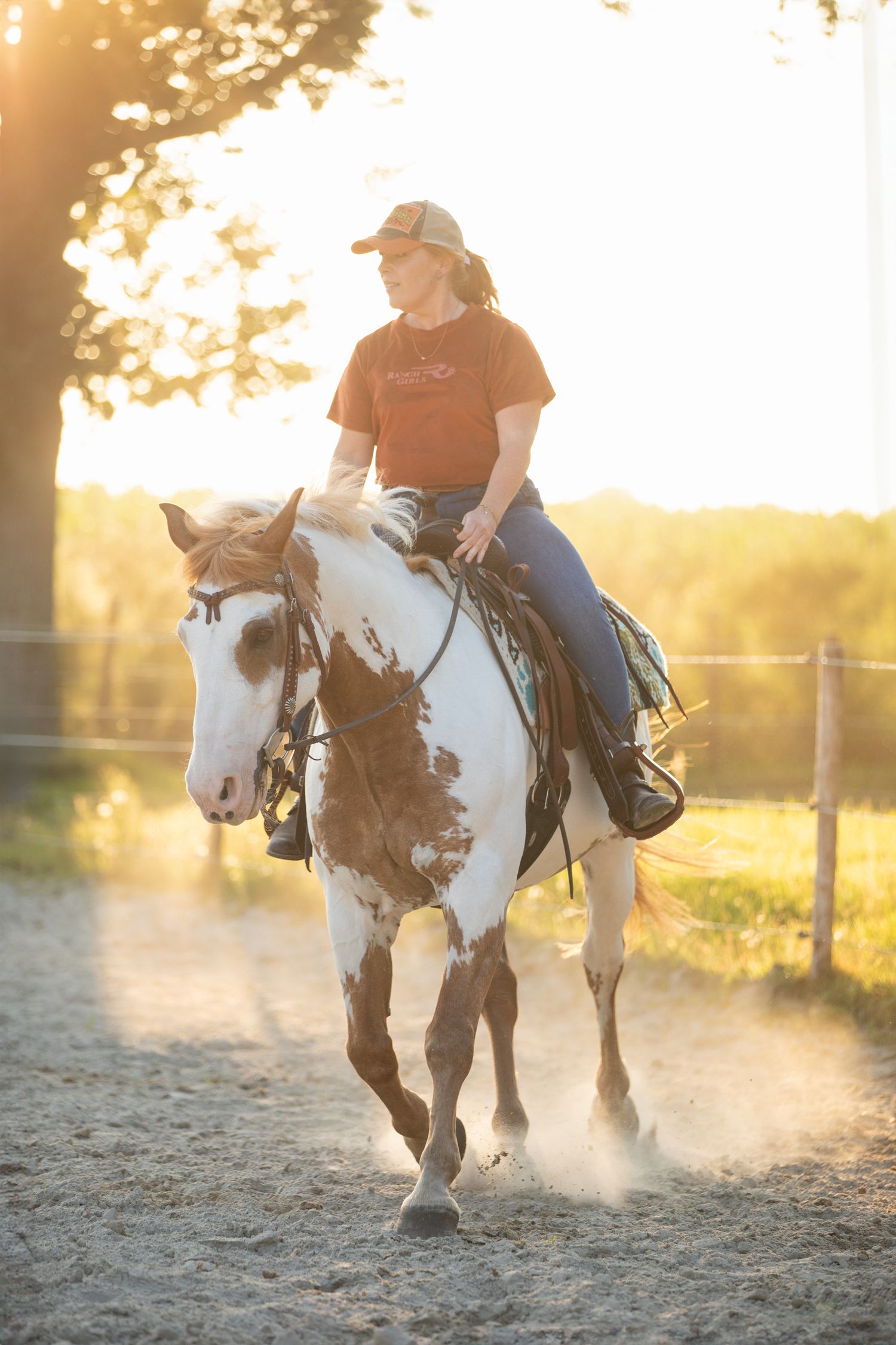 Horse and rider galloping through dusty arena at sunset.