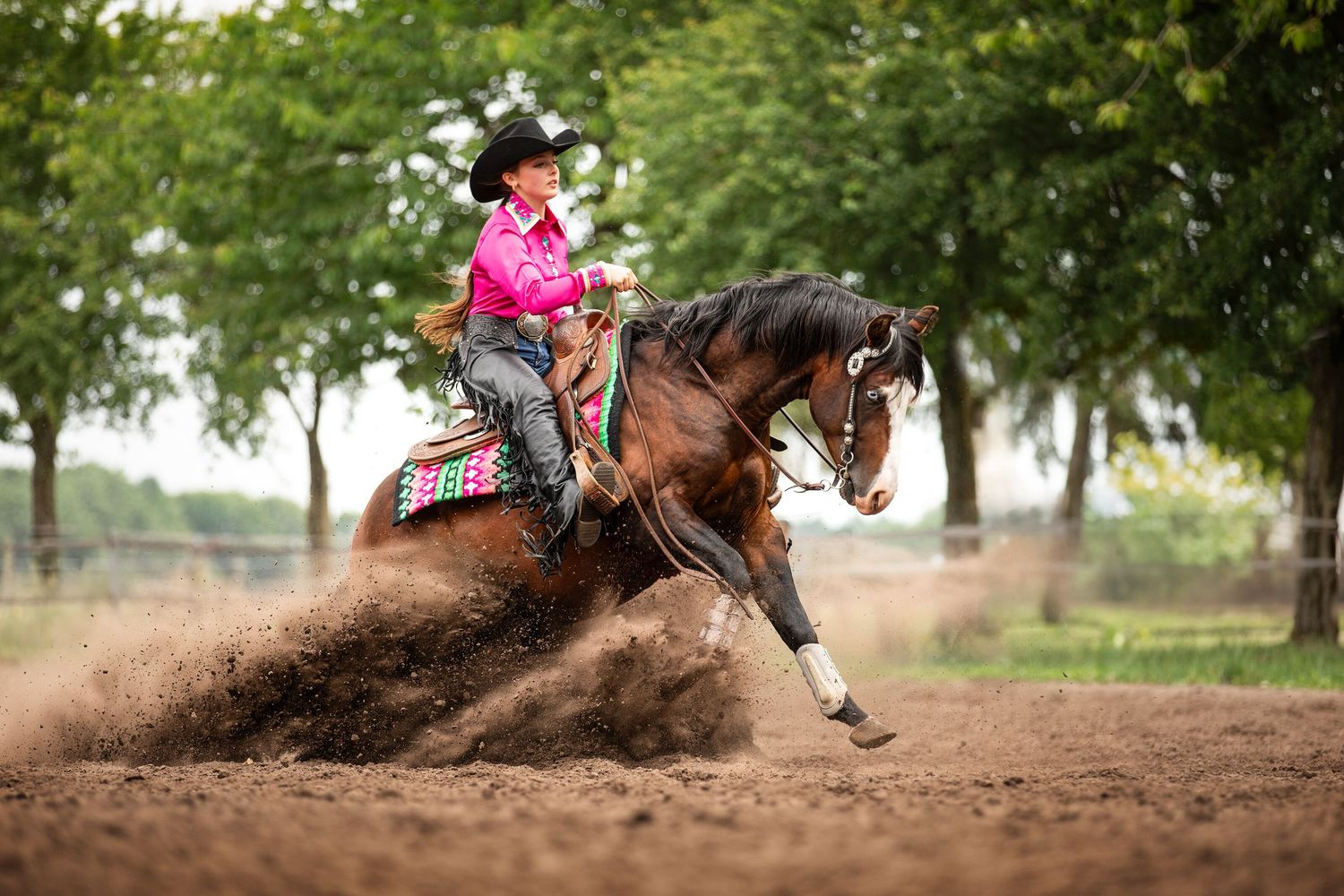 Horse and rider performing a dramatic sliding stop in arena dirt, kicking up dust clouds.