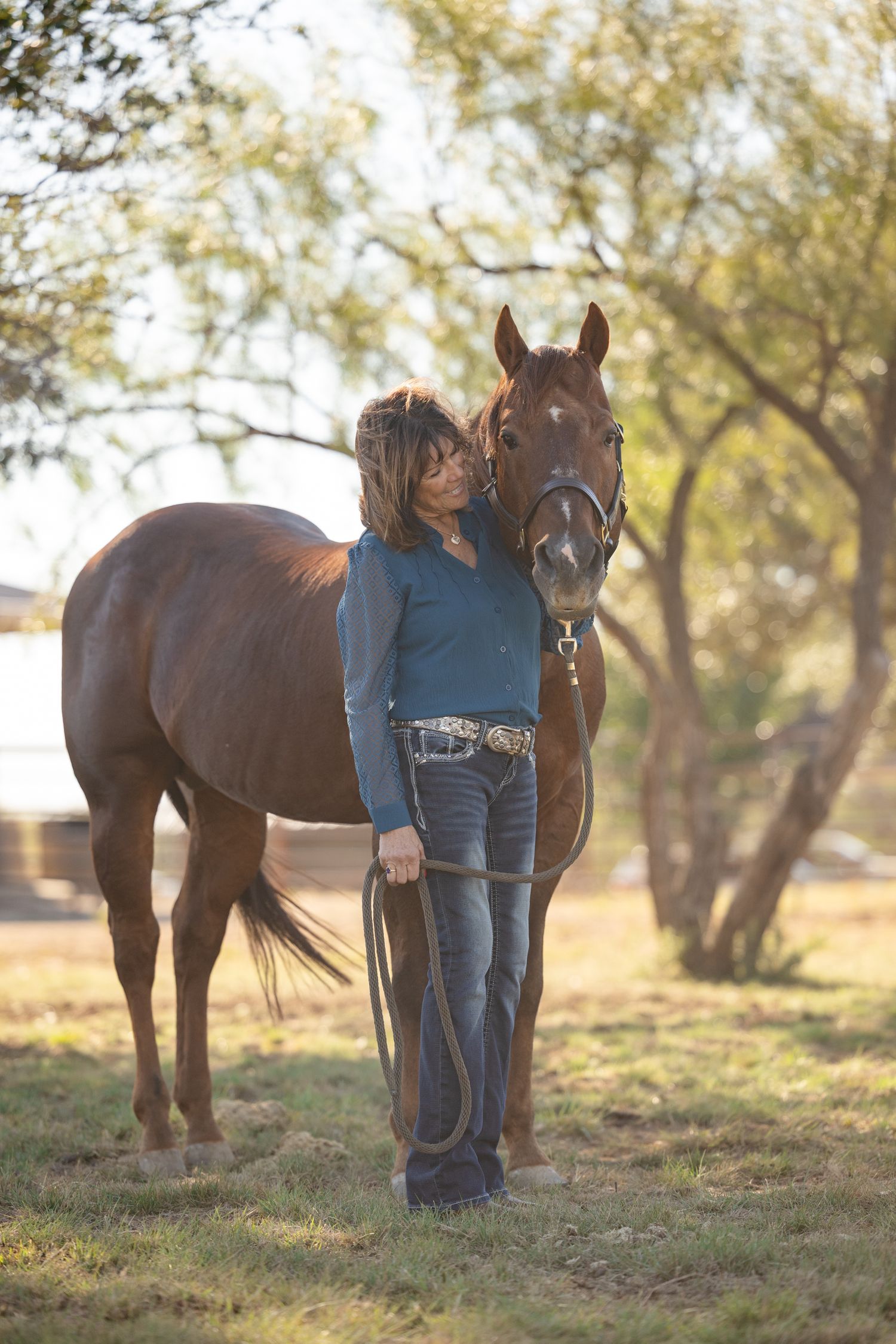Person and horse standing together in a grassy field during golden hour.