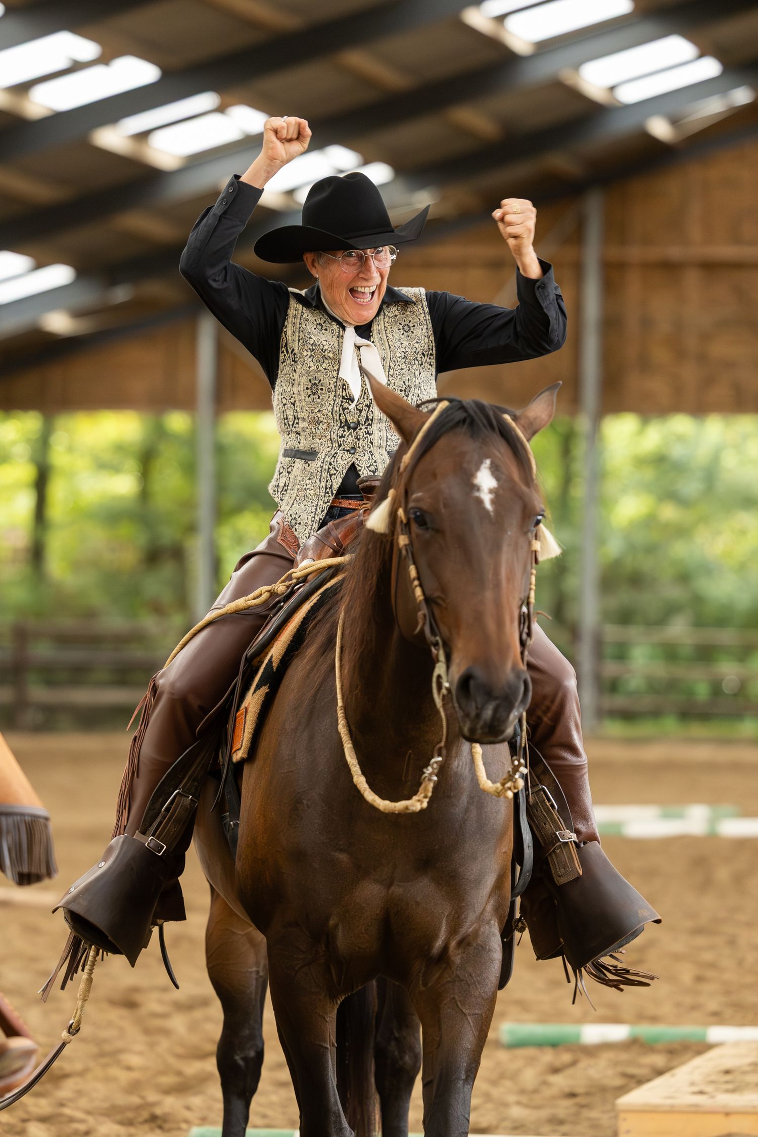 Enthusiastic rider celebrating on horseback during indoor equestrian event.