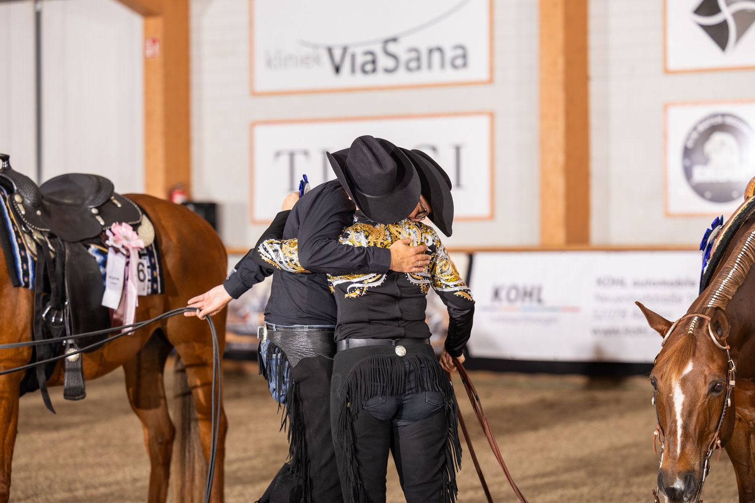 Indoor equestrian arena with sponsor banners and horses lined up for competition.
