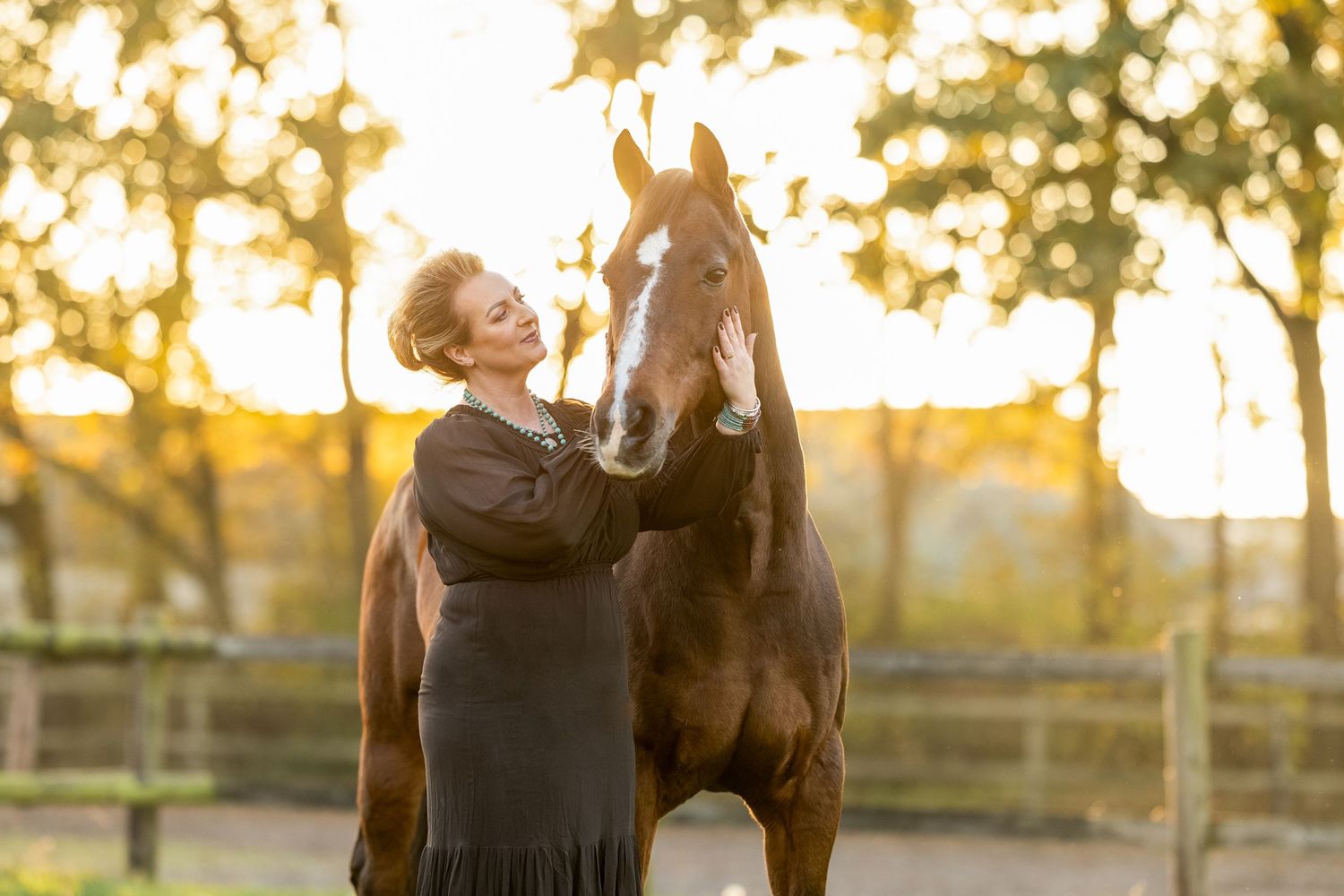 Horse and person in black dress share playful moment in field during sunset.