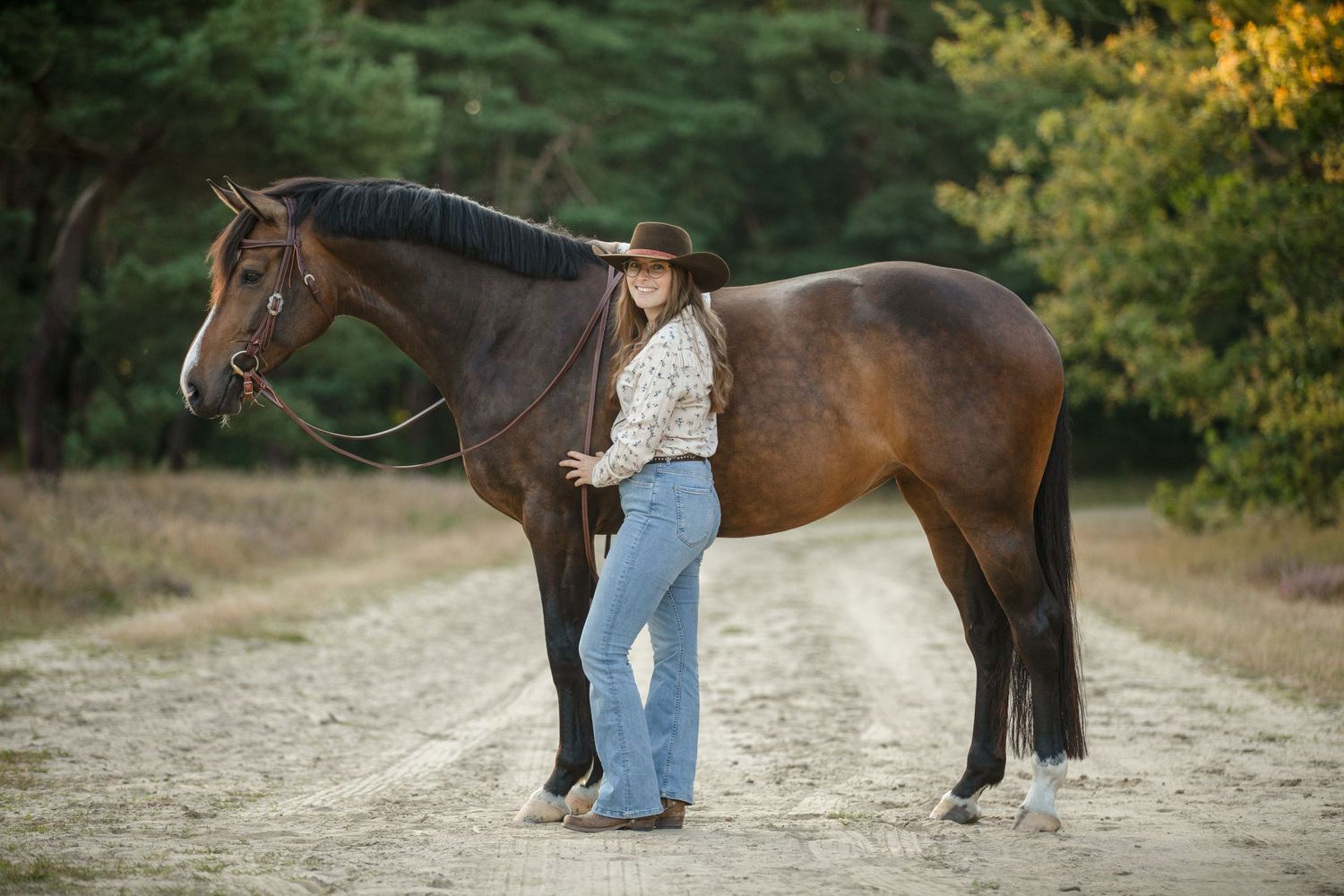 Horse and rider pose on dirt trail with autumn foliage in background.