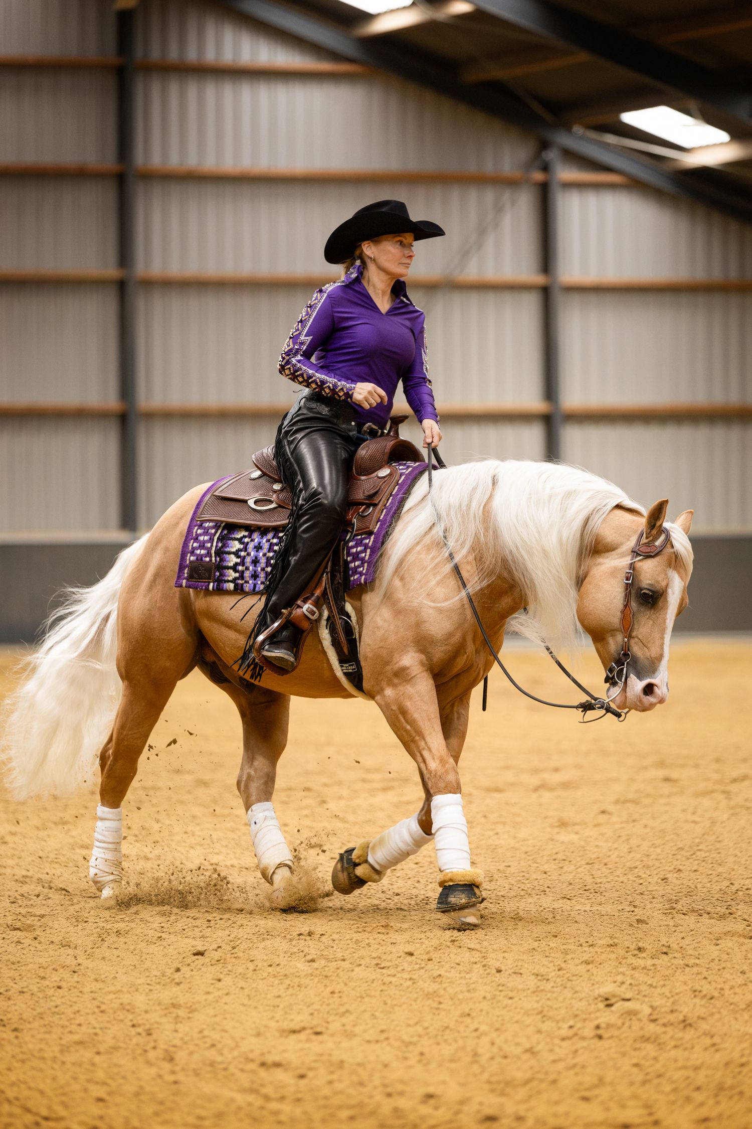 Western rider guiding palomino horse through reining pattern in indoor arena.