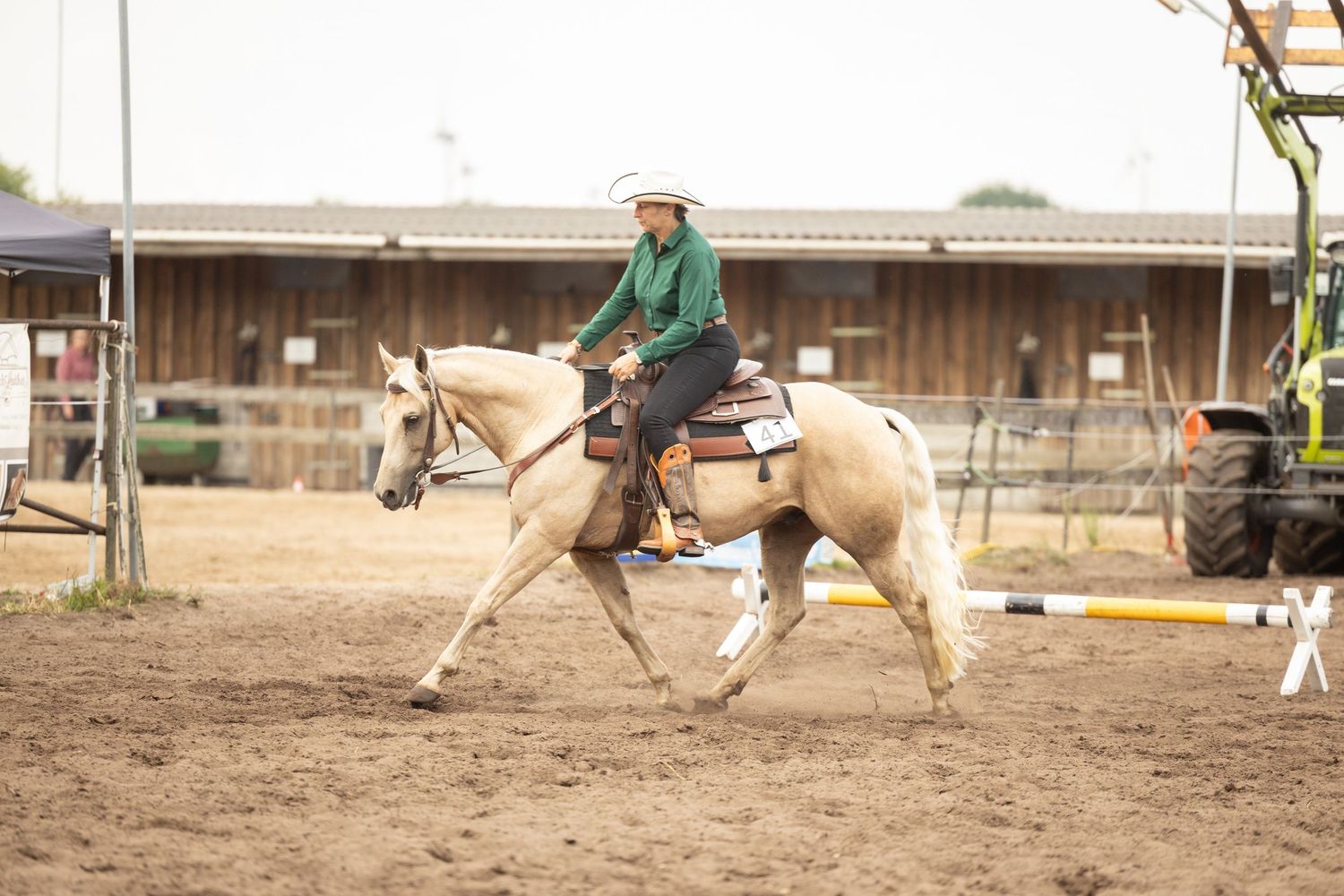 Equestrian rider practicing ranch riding maneuvers on a light-colored horse in an outdoor arena.