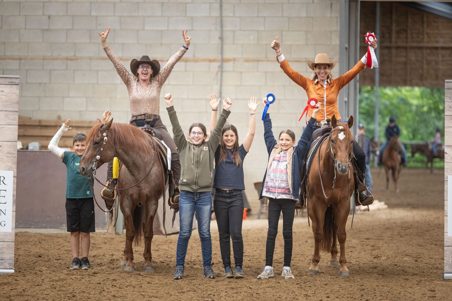 Group of riders on horses celebrating victory at an indoor equestrian competition, raising hands in triumph.