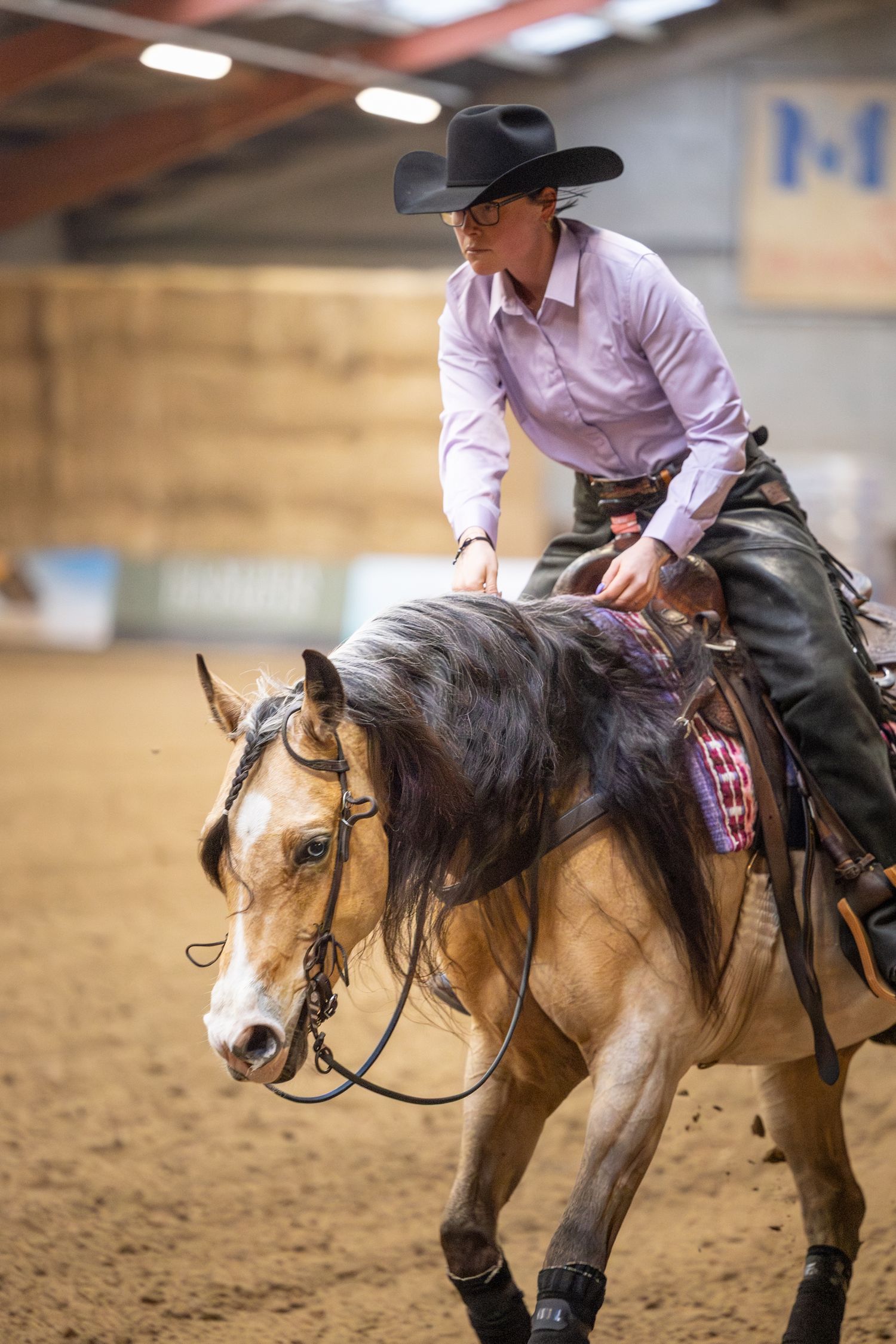 A pinto horse and rider execute a reining pattern in an indoor equestrian arena.