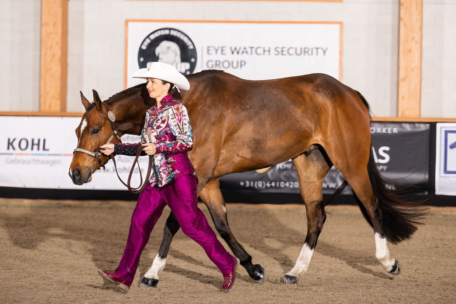 Horse and rider demonstrate a western riding pattern in a sandy indoor arena.