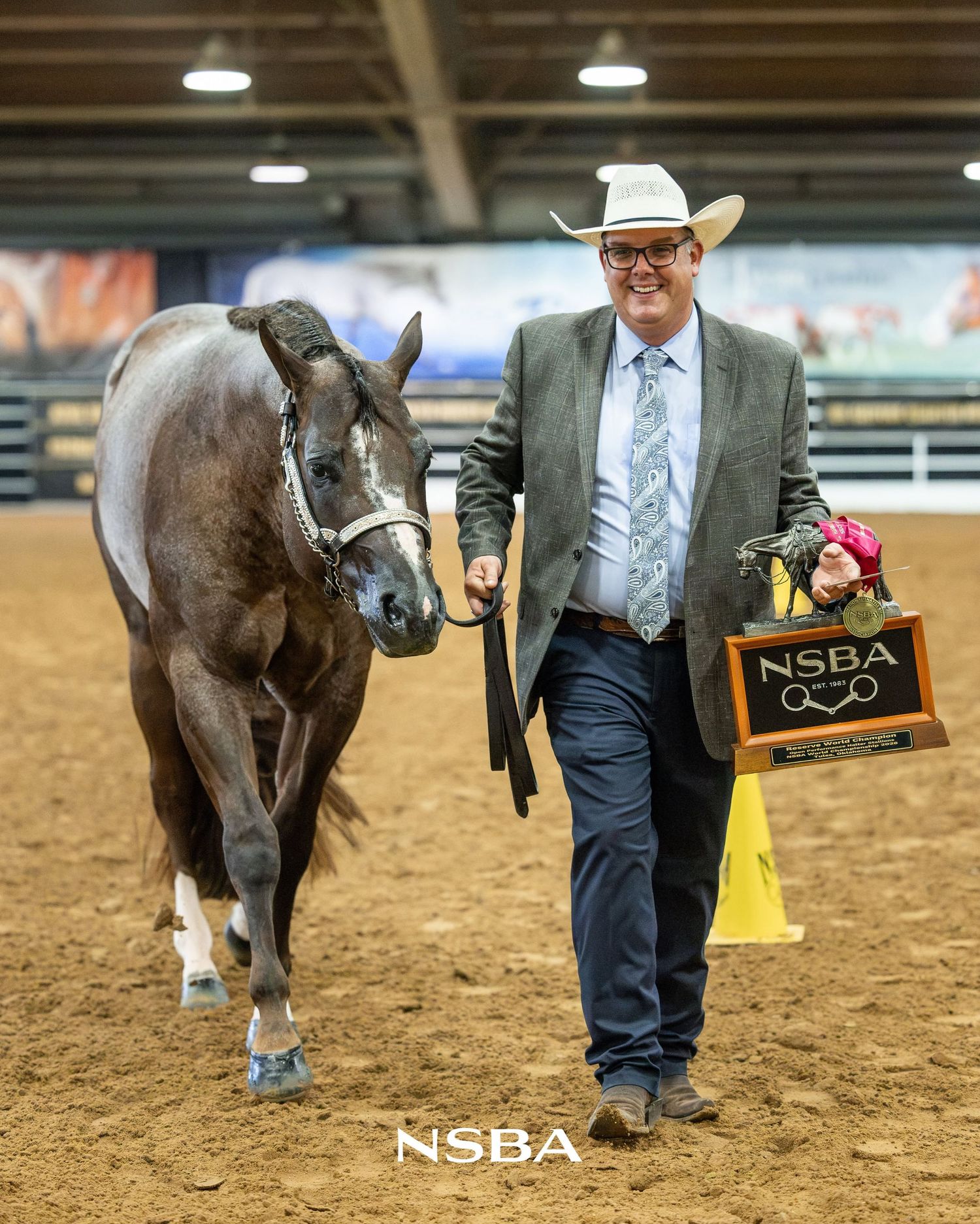 Man in cowboy hat leads AQHA stallion First Thingz First at the NSBA World Show, holding a reserve champion trophy award in indoor arena.