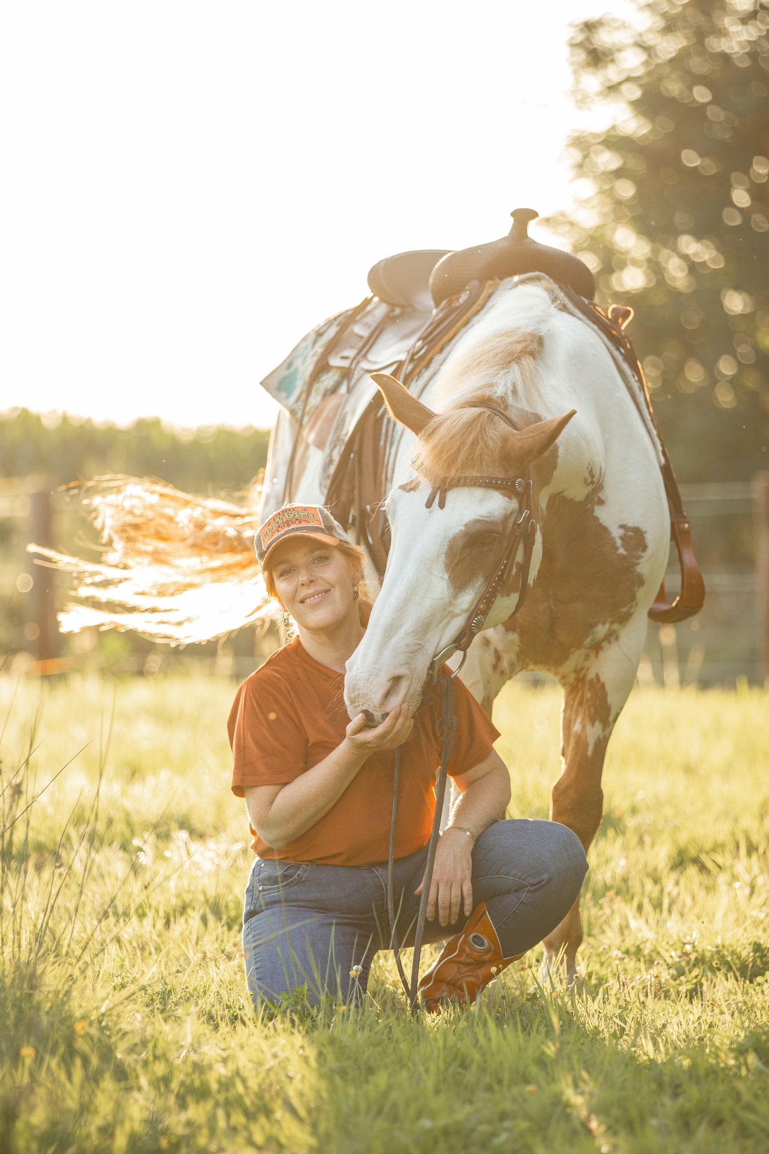 A heartwarming sunset scene shows someone bonding with a paint horse in a grassy field.