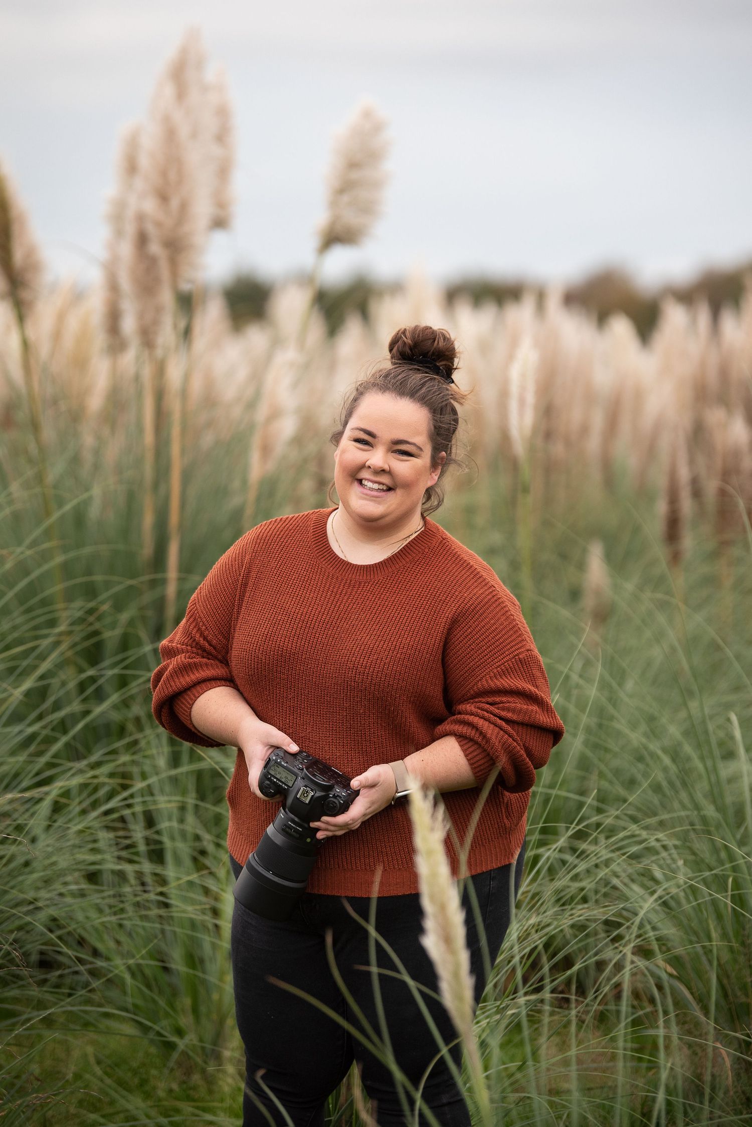 A photographer with camera stands among tall pampas grass in autumn light.