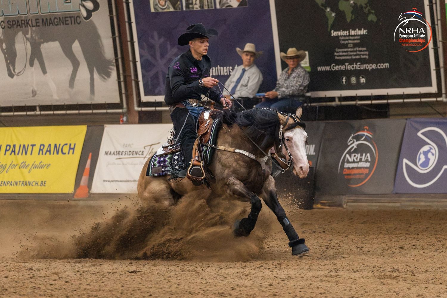 Rider competing in NRHA reining competition, horse performing sliding stop in indoor arena, kicking up dust.