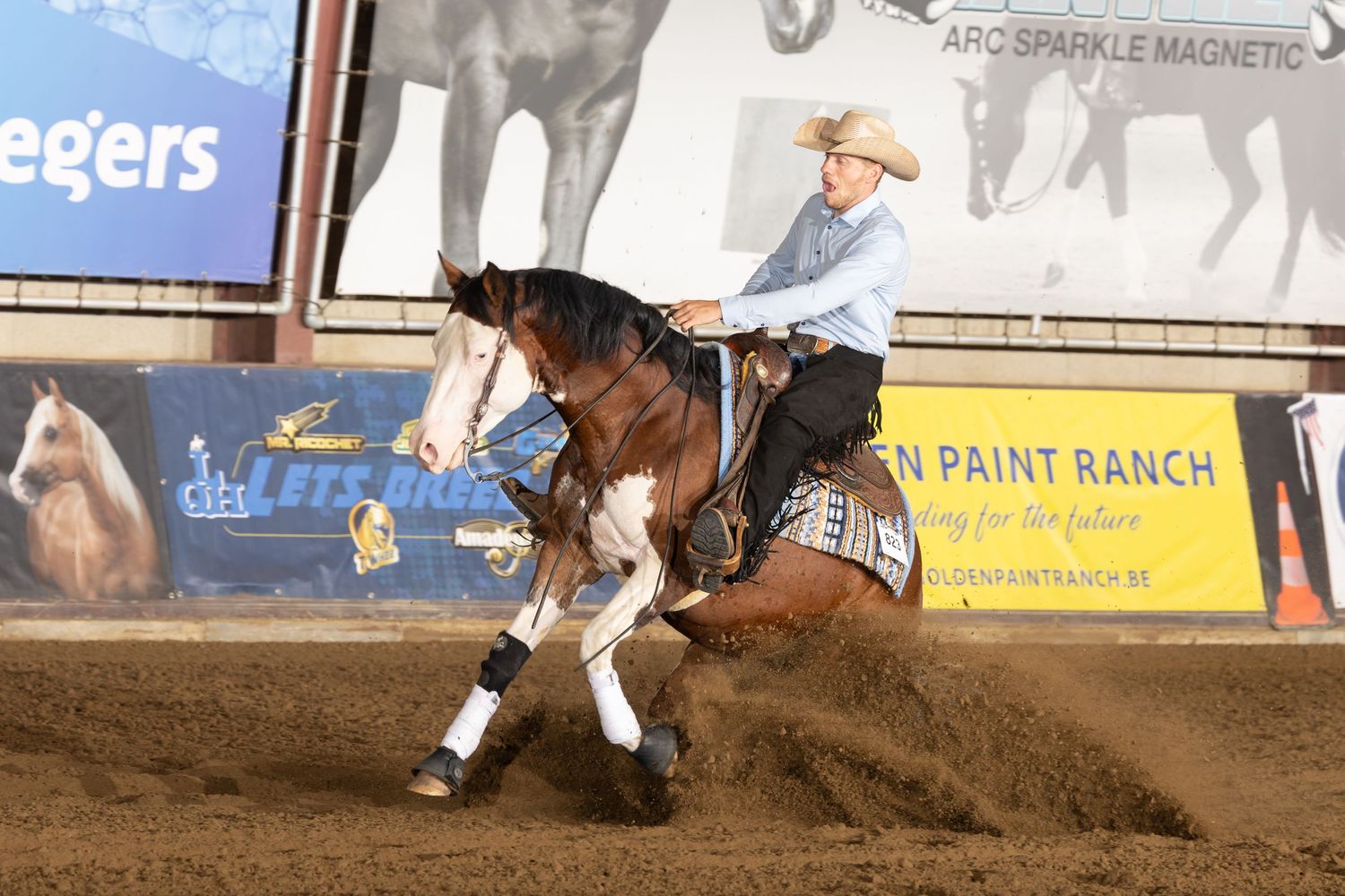 Rider performing a reining maneuver on a paint horse in a dirt arena.