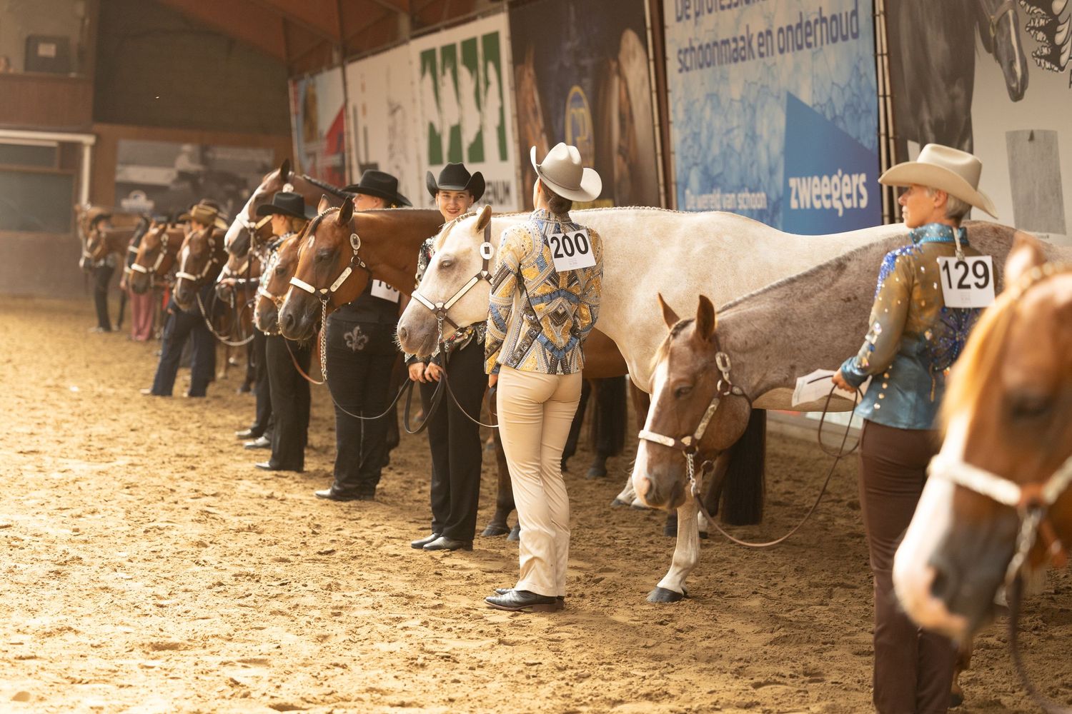 Competitors lined up with their horses during a western show class in an indoor arena.