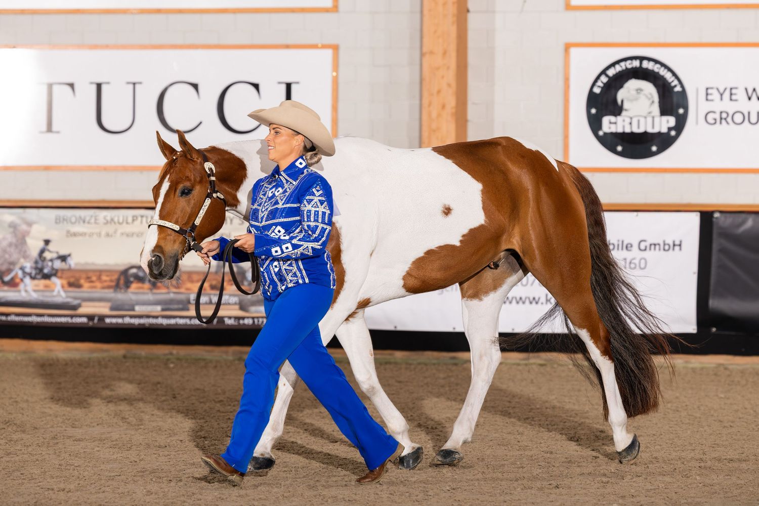 Horses and handlers practicing in an indoor arena with banners and equipment.
