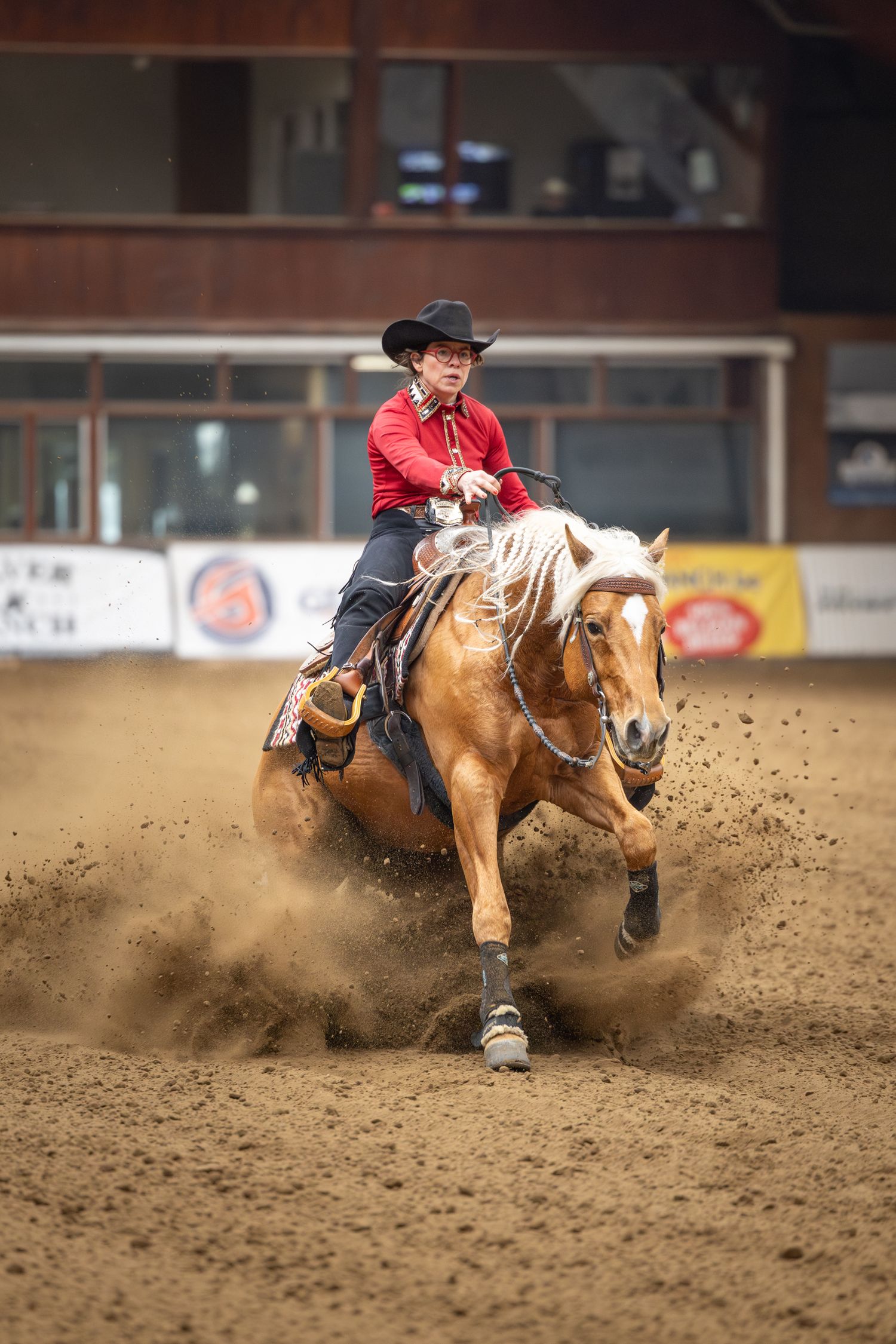 Cowboy rider and horse slide and kick up dirt during dramatic rodeo barrel racing competition in indoor arena.