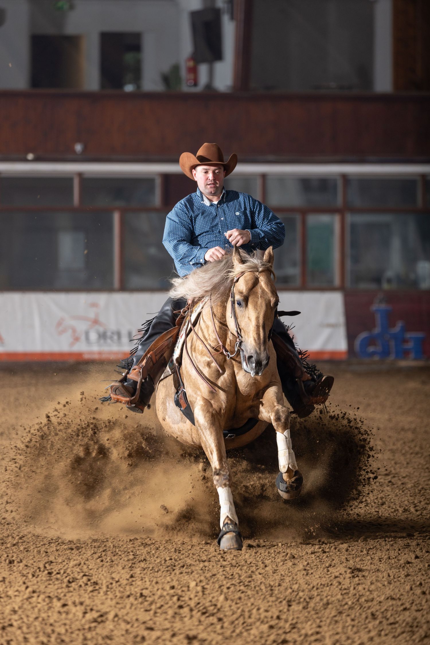 Horse and rider perform sliding stop maneuvers in reining competition, kicking up arena dirt.