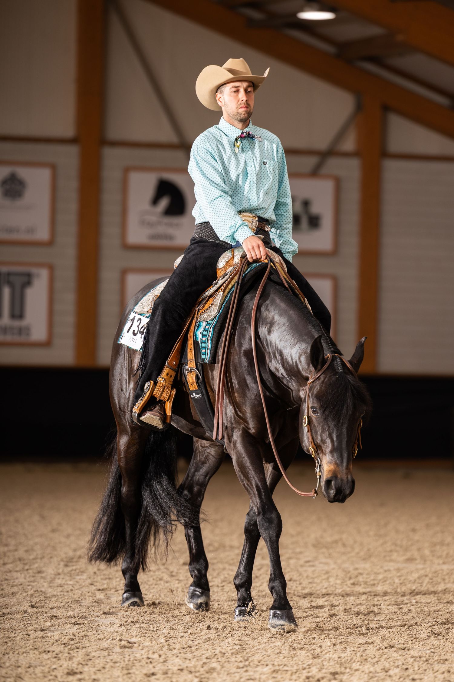 Black pony and rider practicing dressage movements in indoor riding arena.