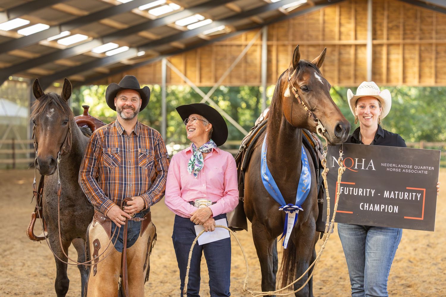 Group of people and horses gathered outside a wooden barn structure.
