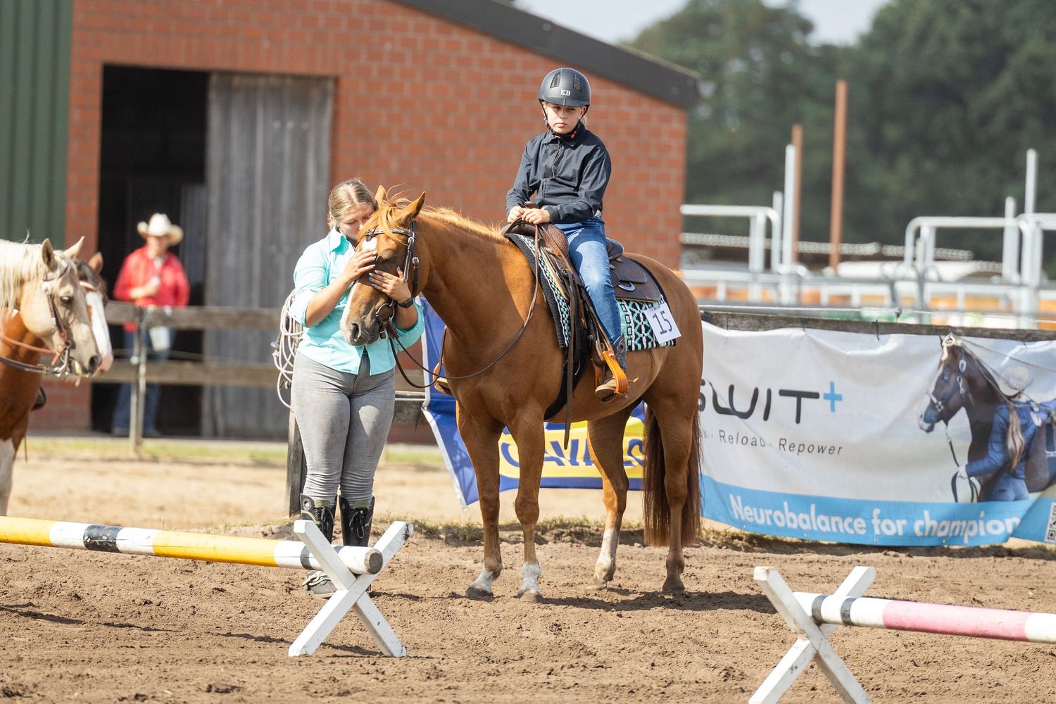 Multiple horses and riders practicing in an outdoor arena with brick building in background.