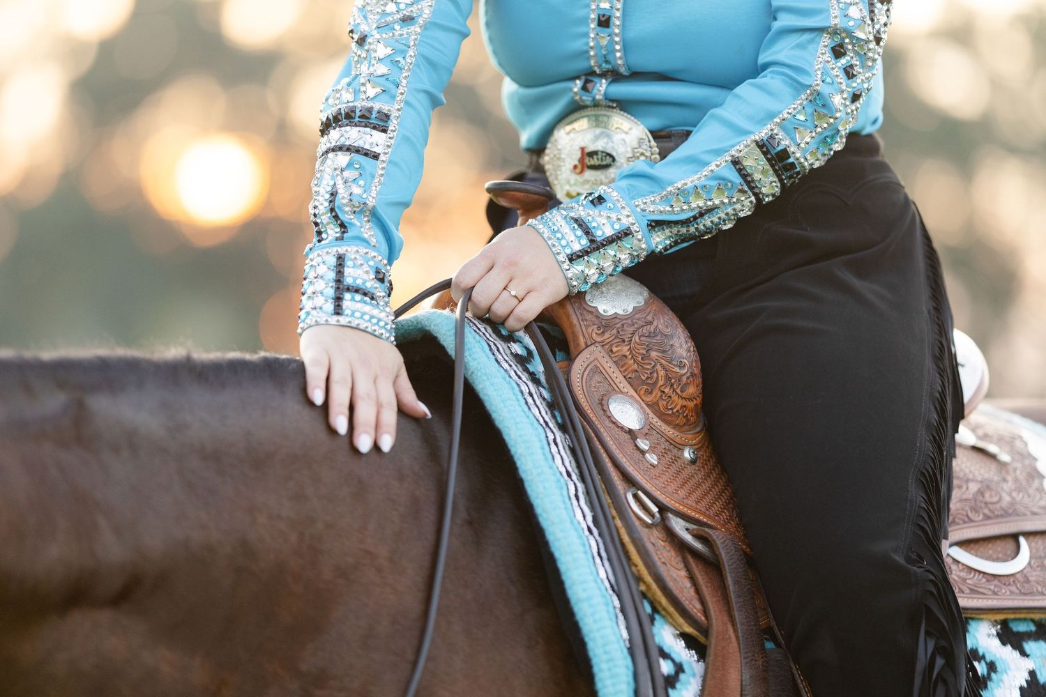Woman in turquoise western shirt riding a horse with decorative leather saddle and black pants.