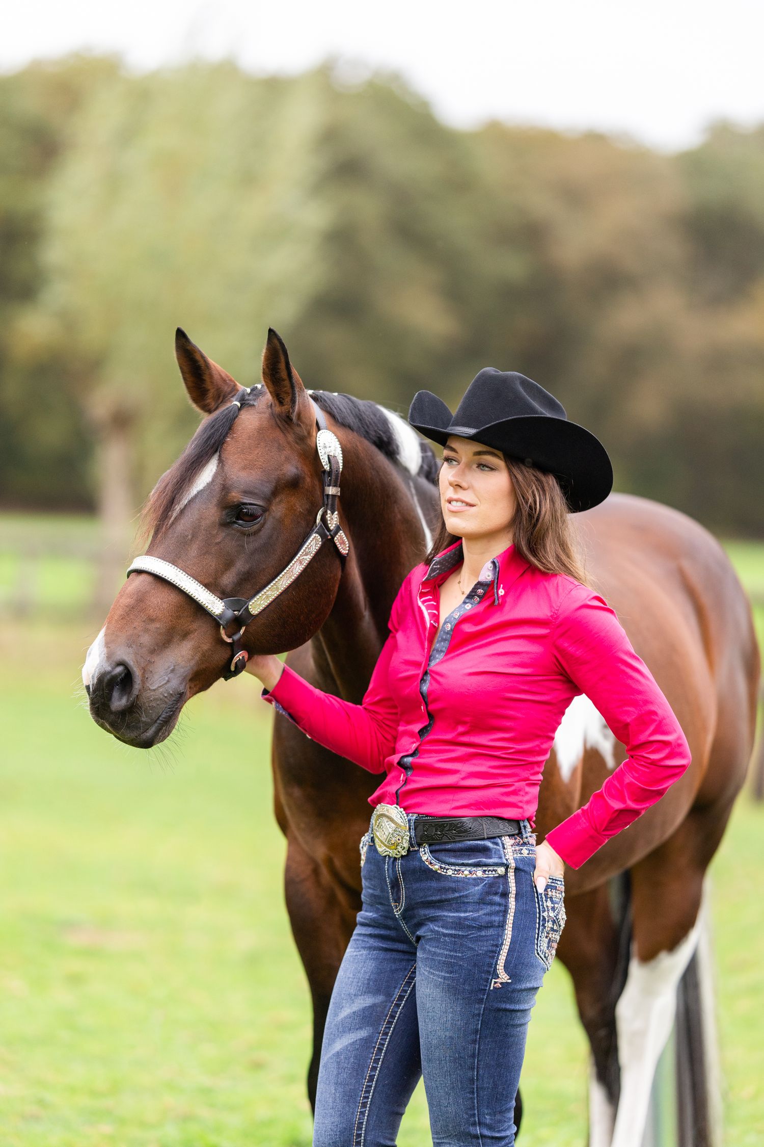Horse and handler in western attire standing in green pasture during fall season.