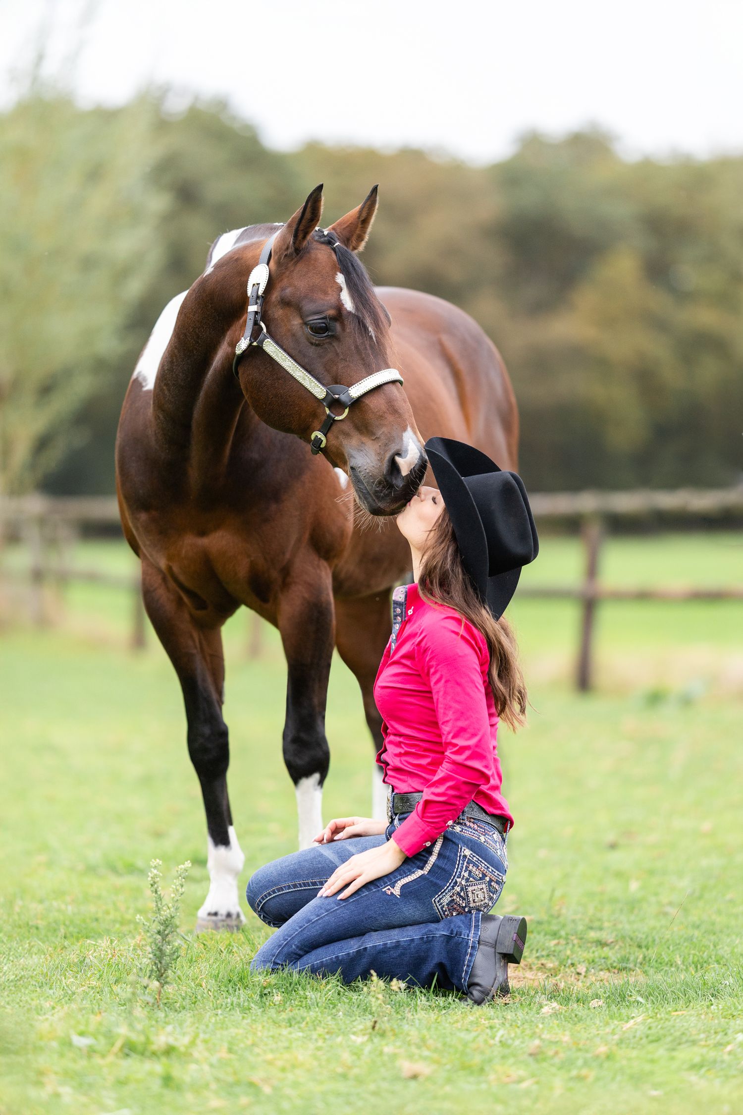Person in pink shirt sitting with brown Paint horse in green field.