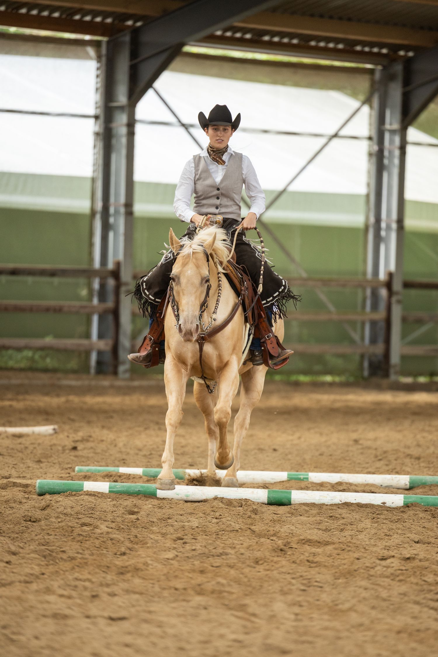 Palomino horse clearing ground pole obstacle in indoor western riding arena.