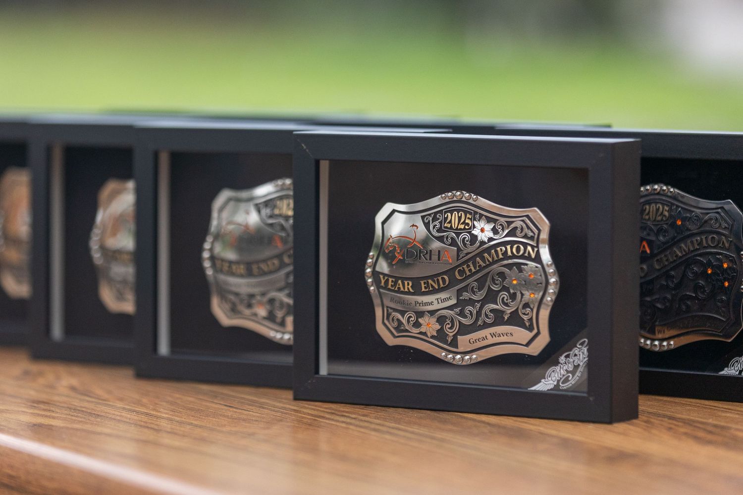 A collection of ornate western belt buckles displayed in black frames on a wooden surface.