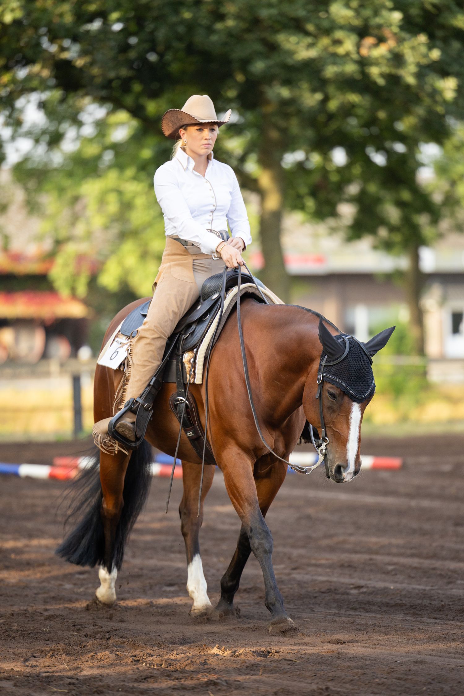 Western rider in tan pants and white shirt competing in an arena on a bay horse.
