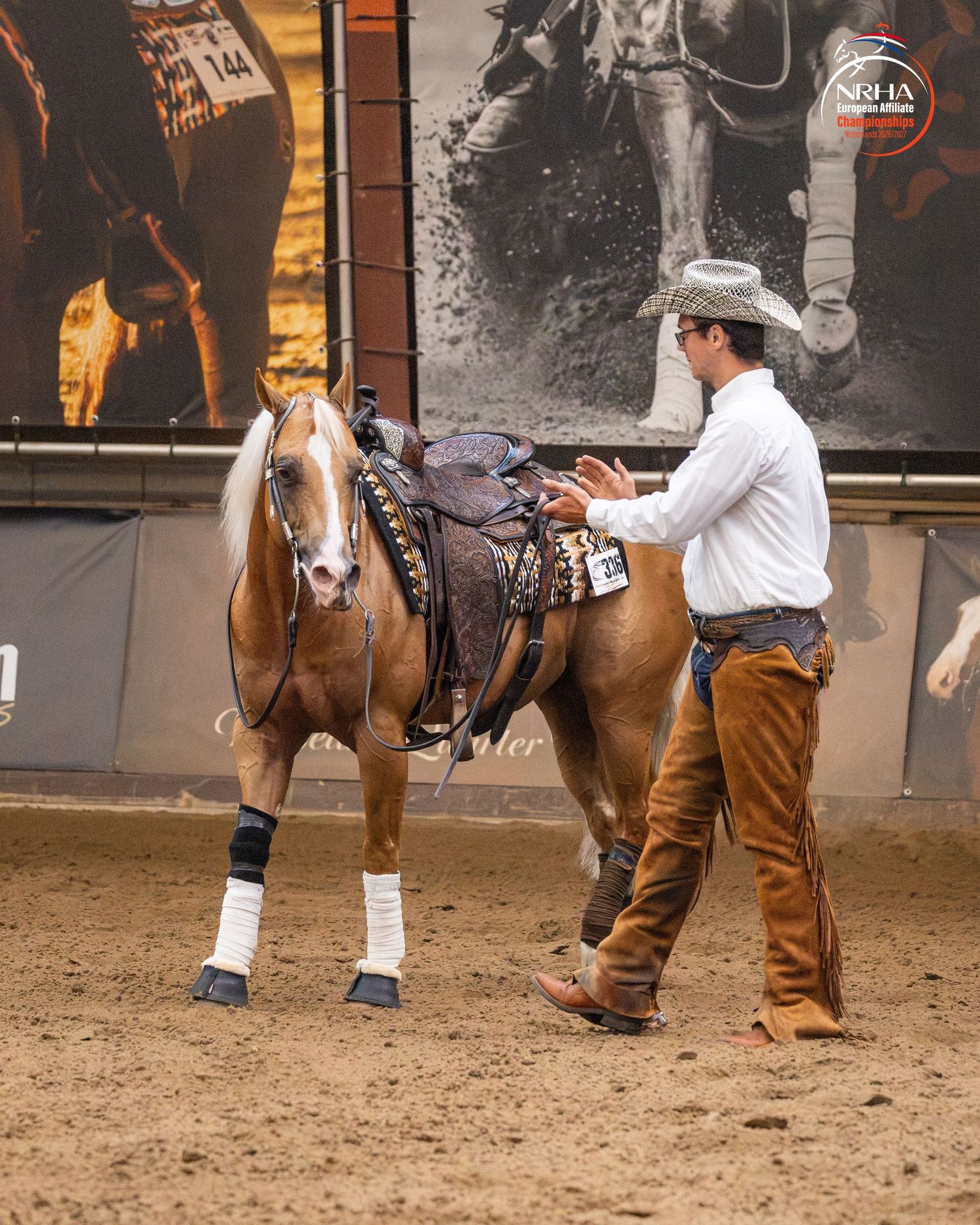 Cowboy in white shirt and hat leads a palomino horse in Western tack at an indoor equestrian competition.
