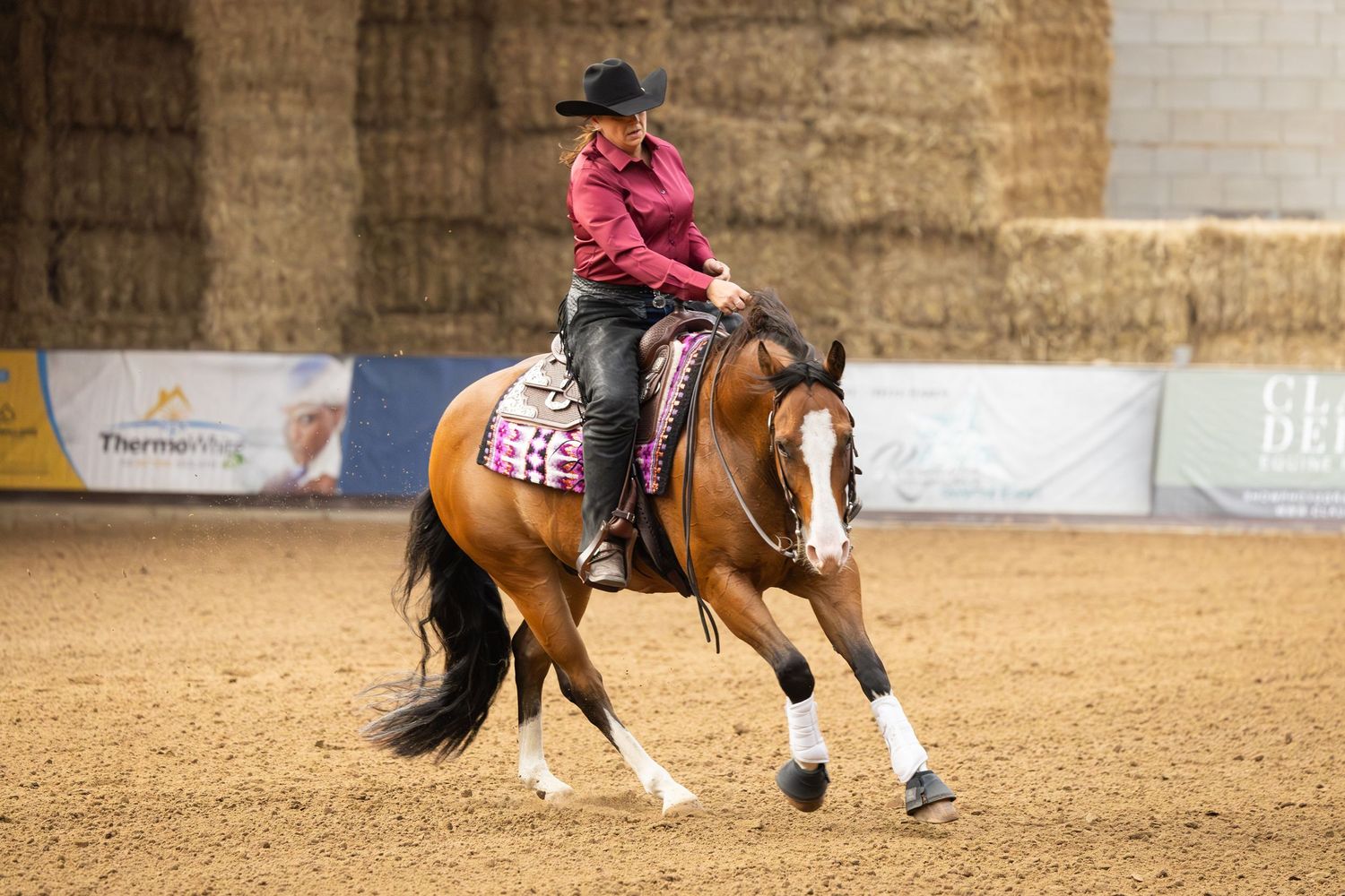 A rider performs a reining pattern on a chestnut horse in a sandy indoor arena.