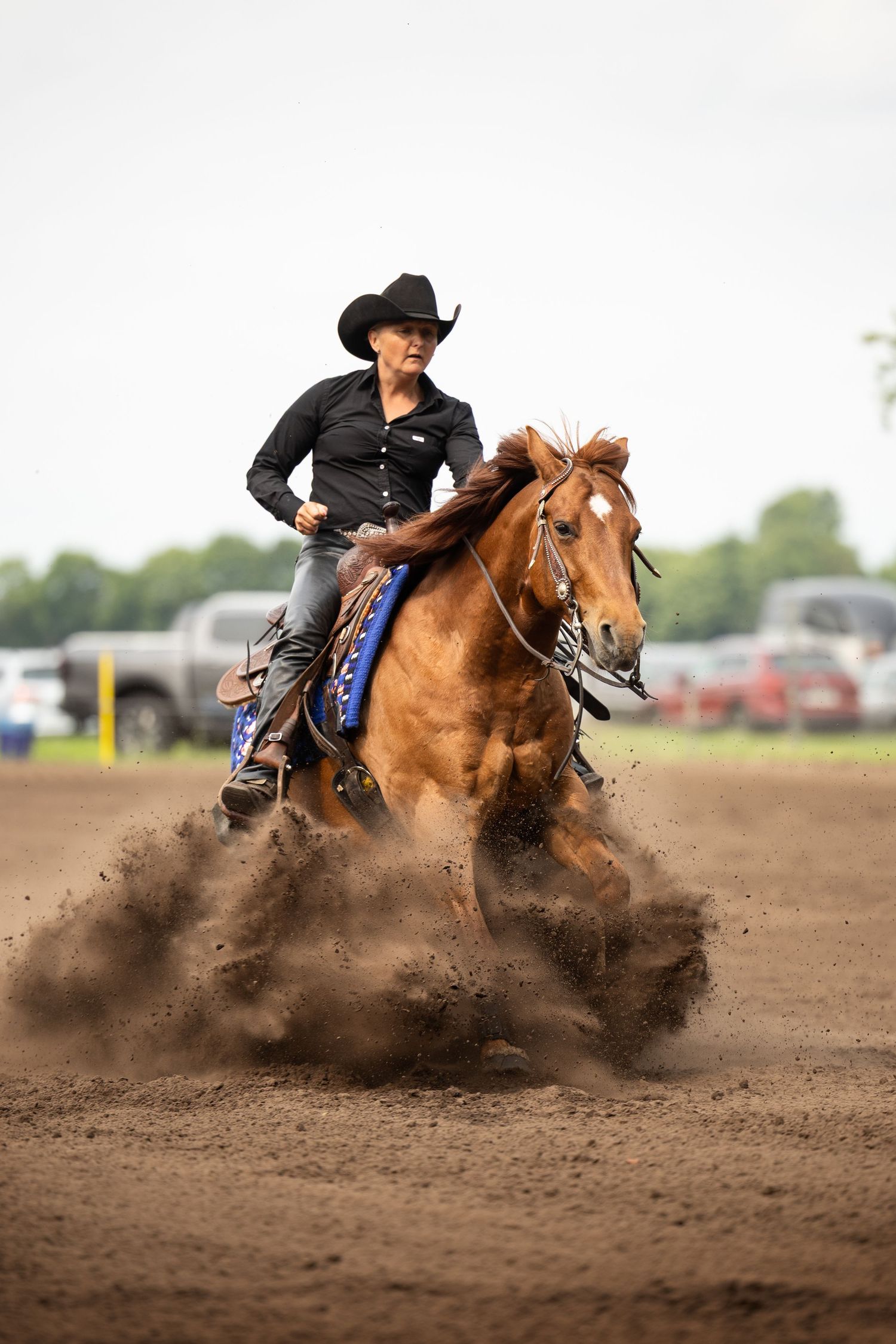 Horse and rider performing sliding stop maneuver in dirt arena creating dramatic dust cloud.