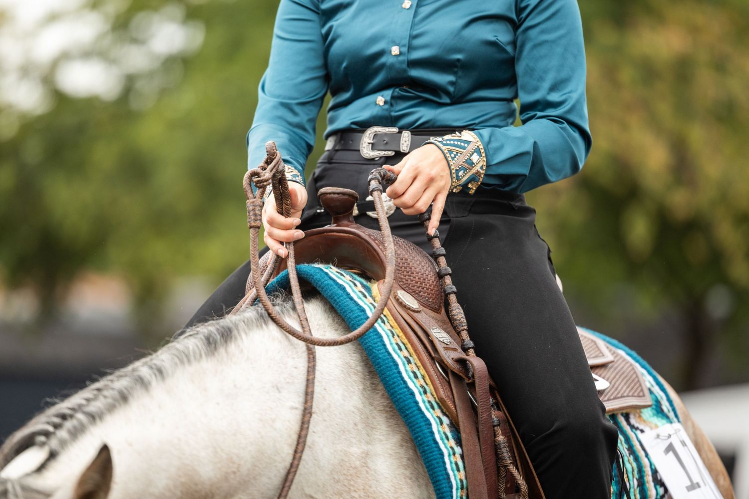 Close-up of hands holding reins while riding a horse with turquoise tack.