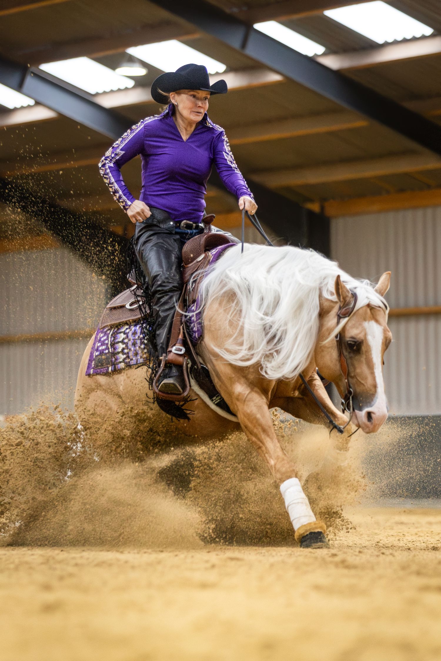 Dynamic action shot of reining horse performing sliding stop with sand spraying in indoor arena.