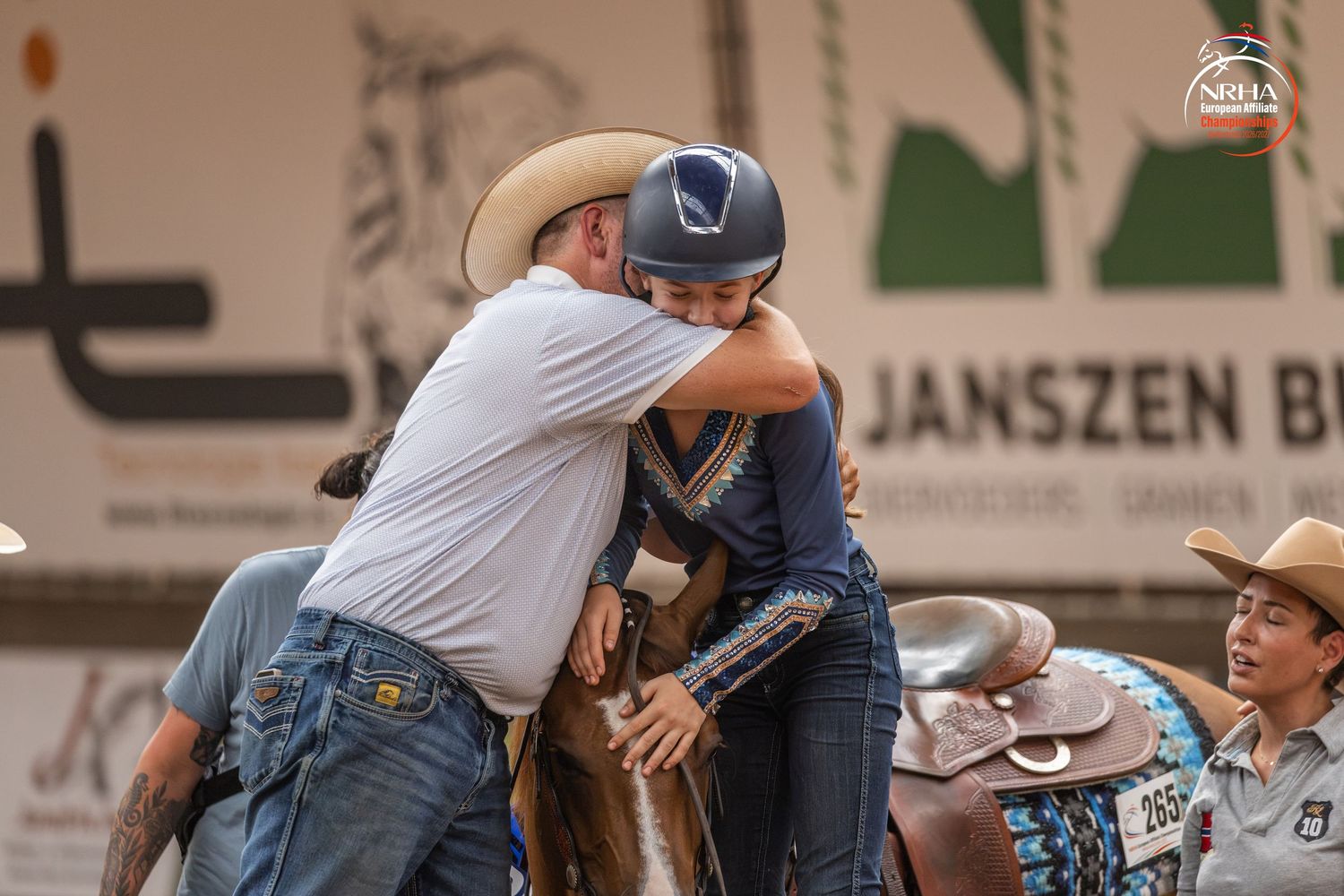 Cowboy hugging a young equestrian rider on horseback at an indoor rodeo arena competition.