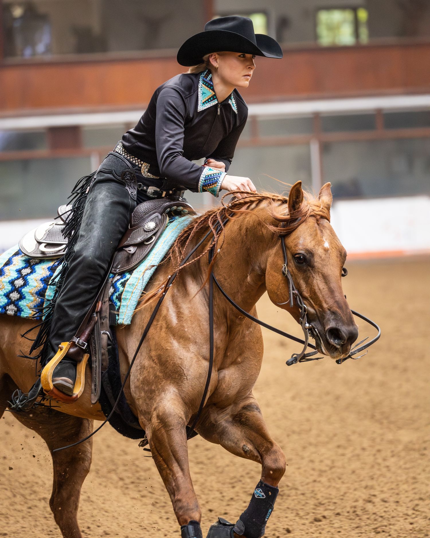 Chestnut quarter horse and rider compete in western riding event with turquoise saddle blanket.