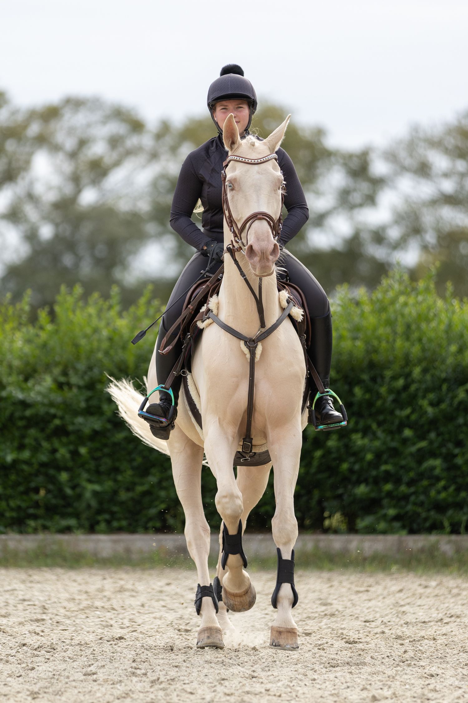 A cream-colored horse and rider performing dressage movements in a sandy arena.