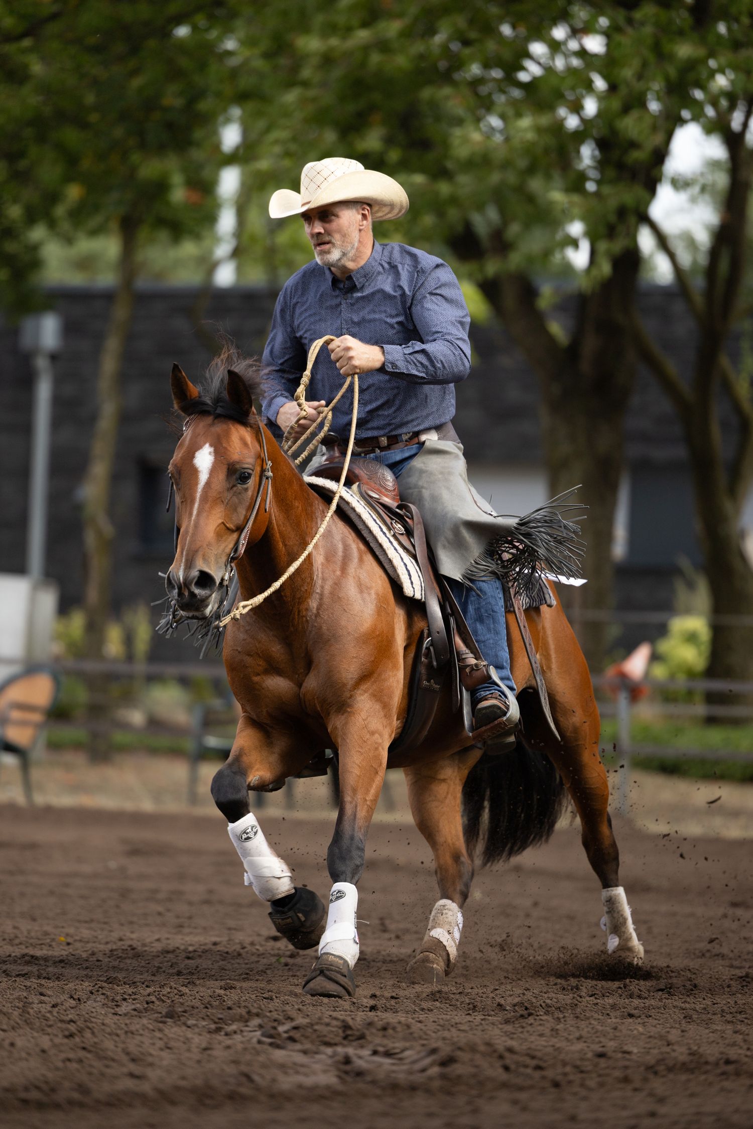 Brown horse galloping through dirt arena during western riding competition.