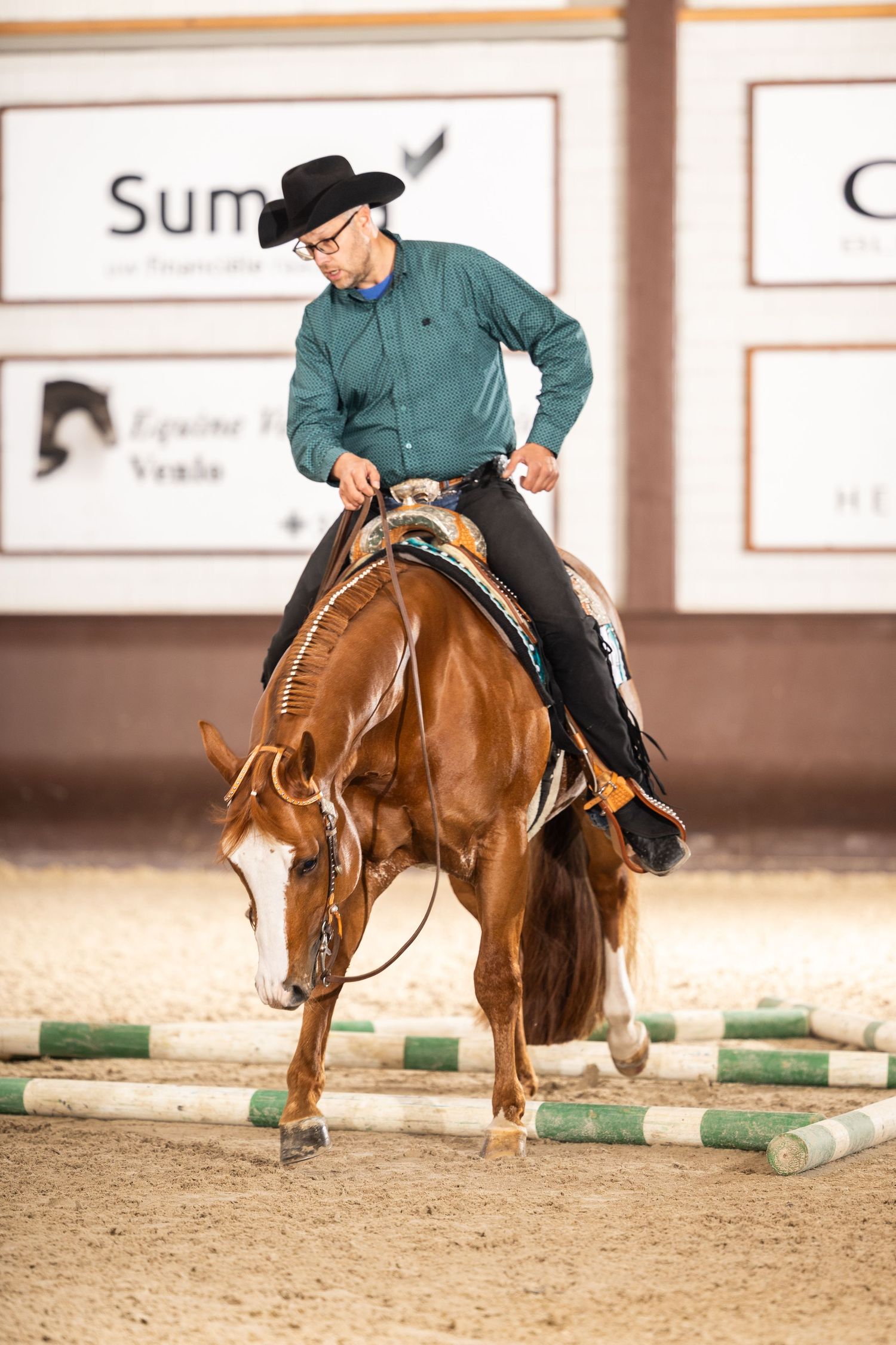 Horse and rider executing dressage patterns around green ground markers in an indoor arena.