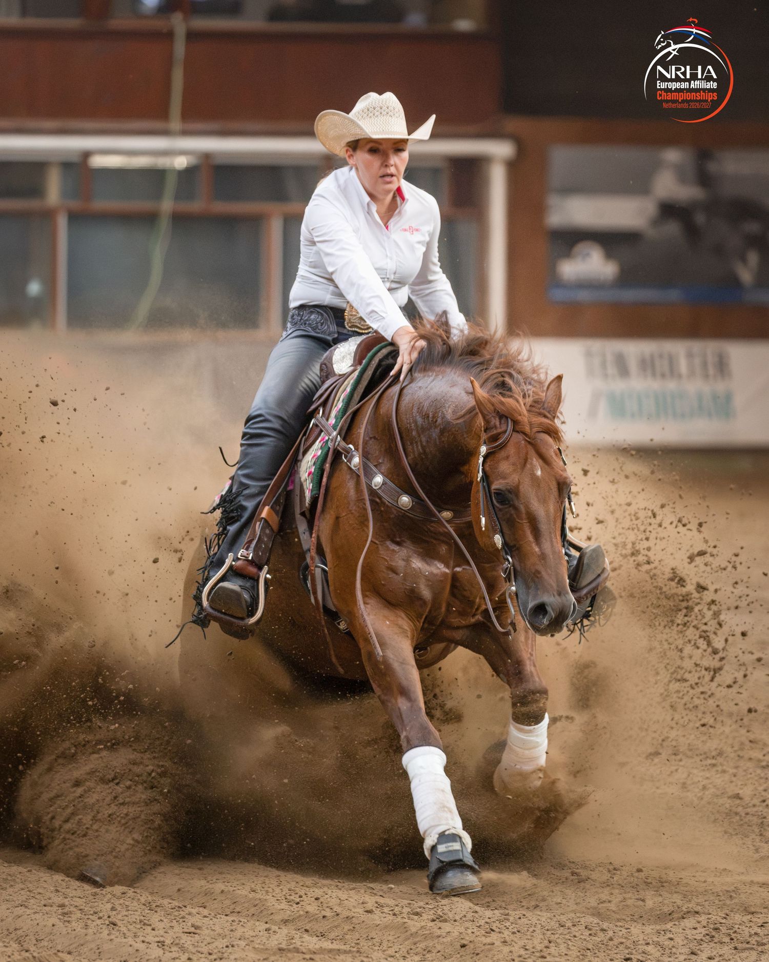Cowgirl riding a chestnut horse performing a sliding stop in a dusty rodeo arena.