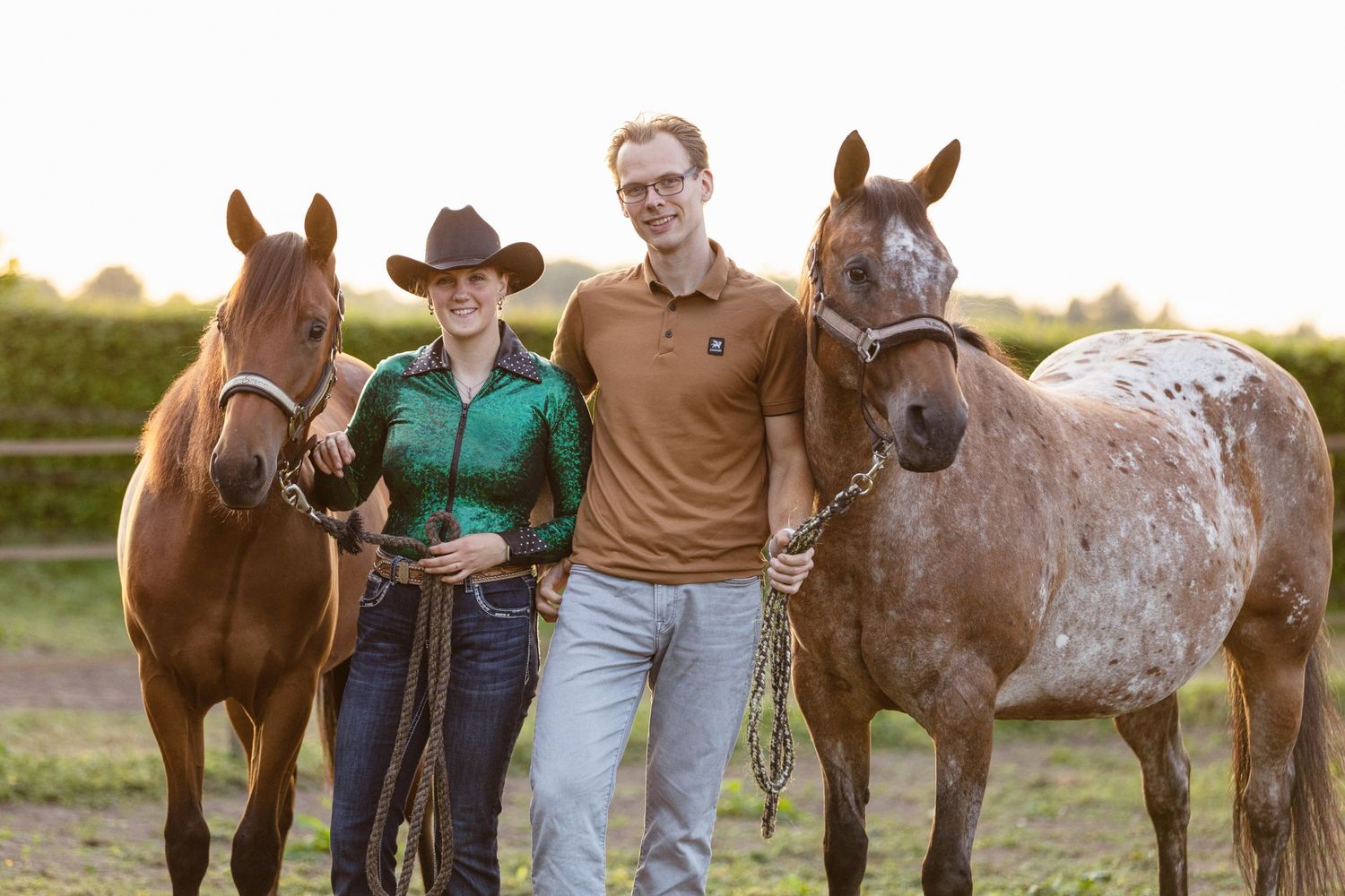 Horses and handlers gather in a grassy field at sunset.