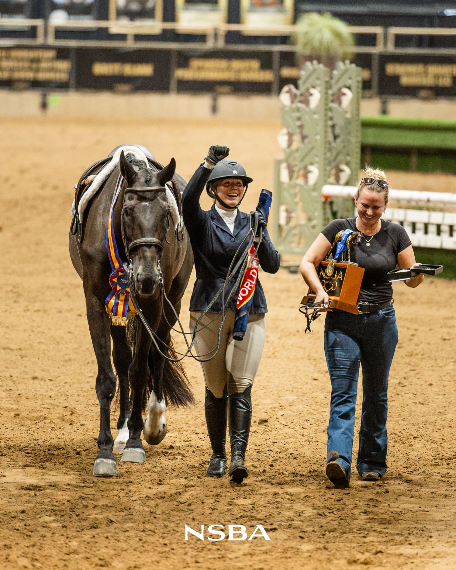 A smiling equestrian rider celebrates with raised fist beside a gray horse at an the NSBA World Show