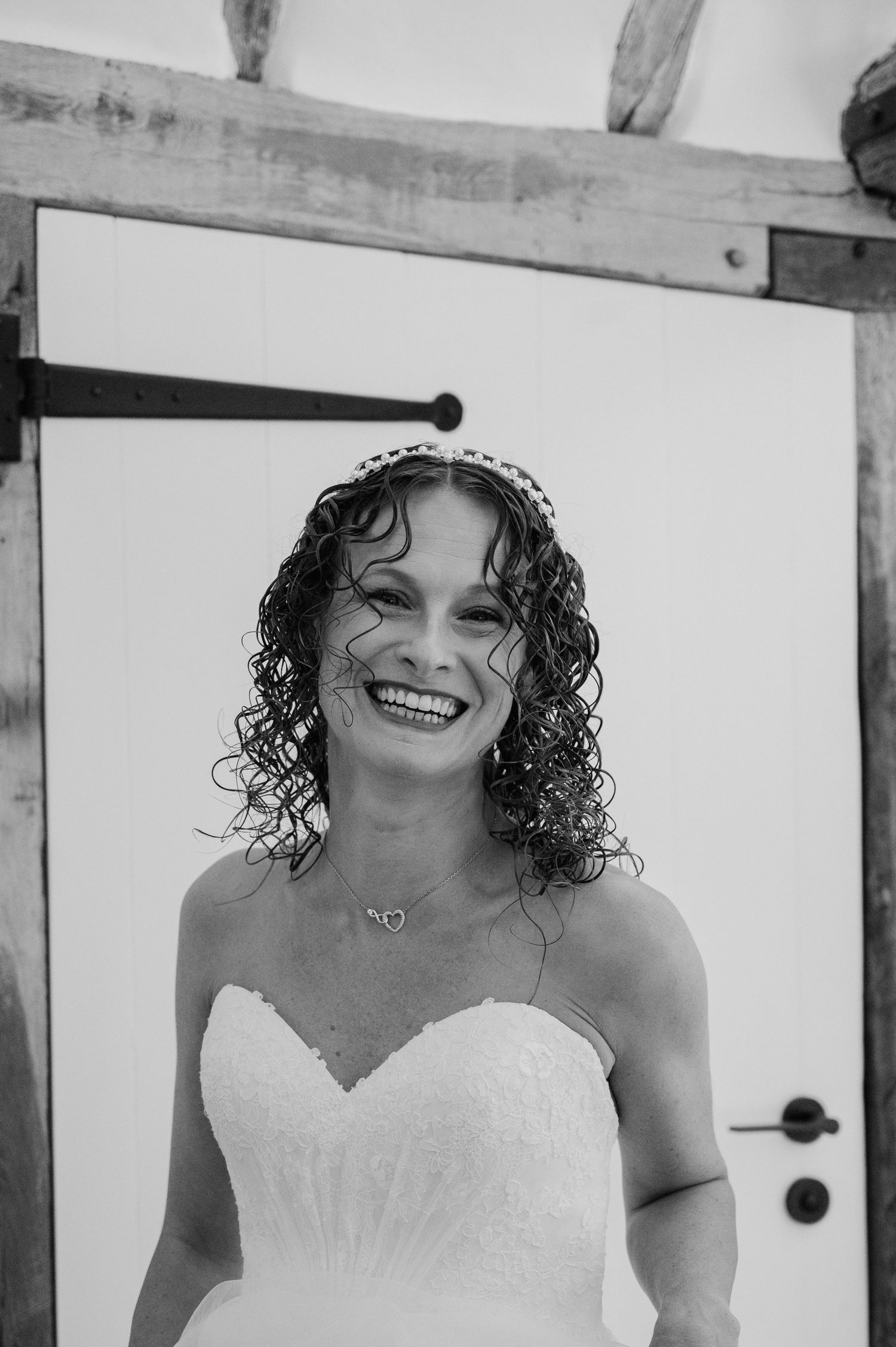 Radiant bride with curly hair and tiara smiles joyfully in black and white wedding portrait.