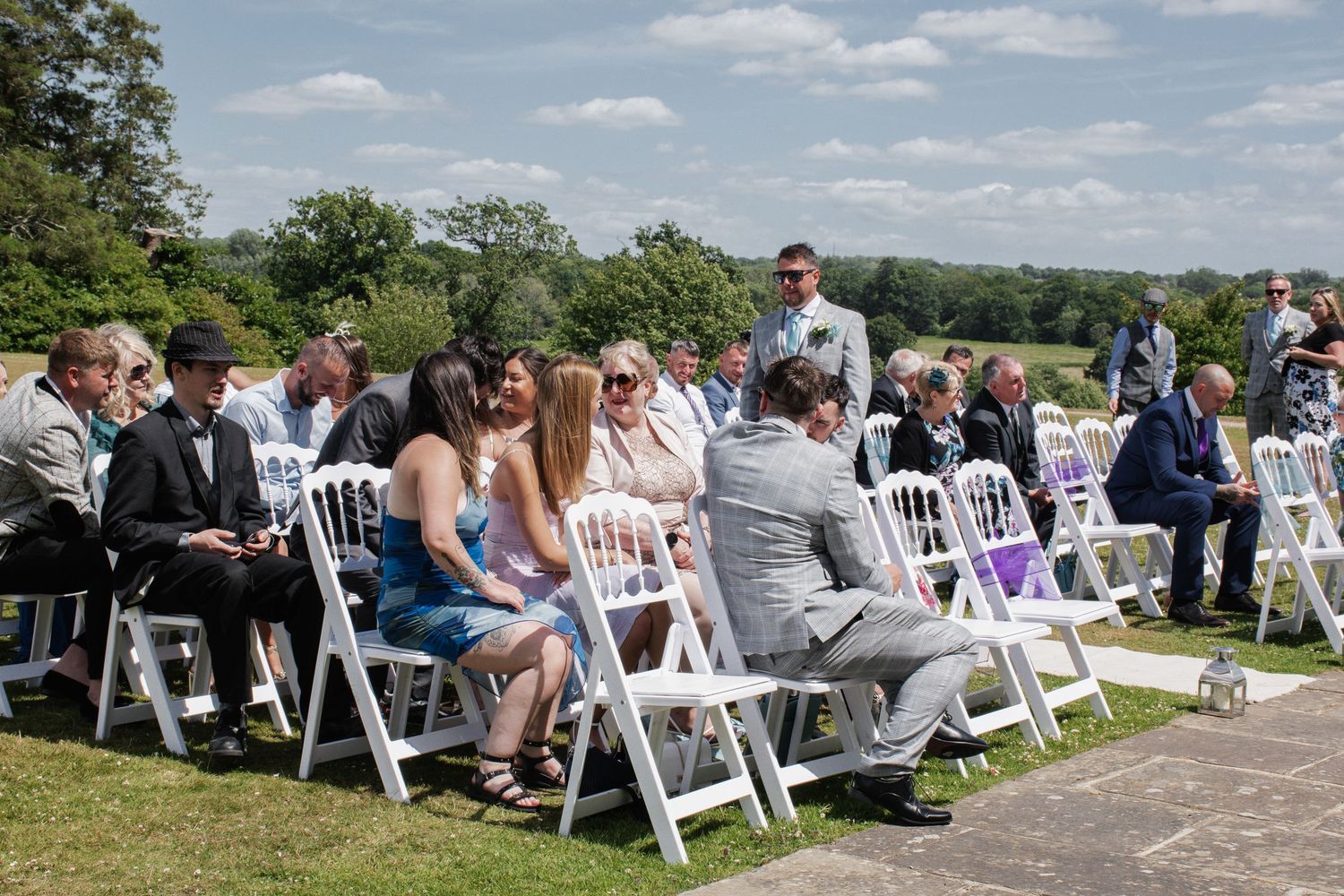 Wedding guests seated on white chairs outdoors on a sunny day for an elegant garden wedding ceremony.