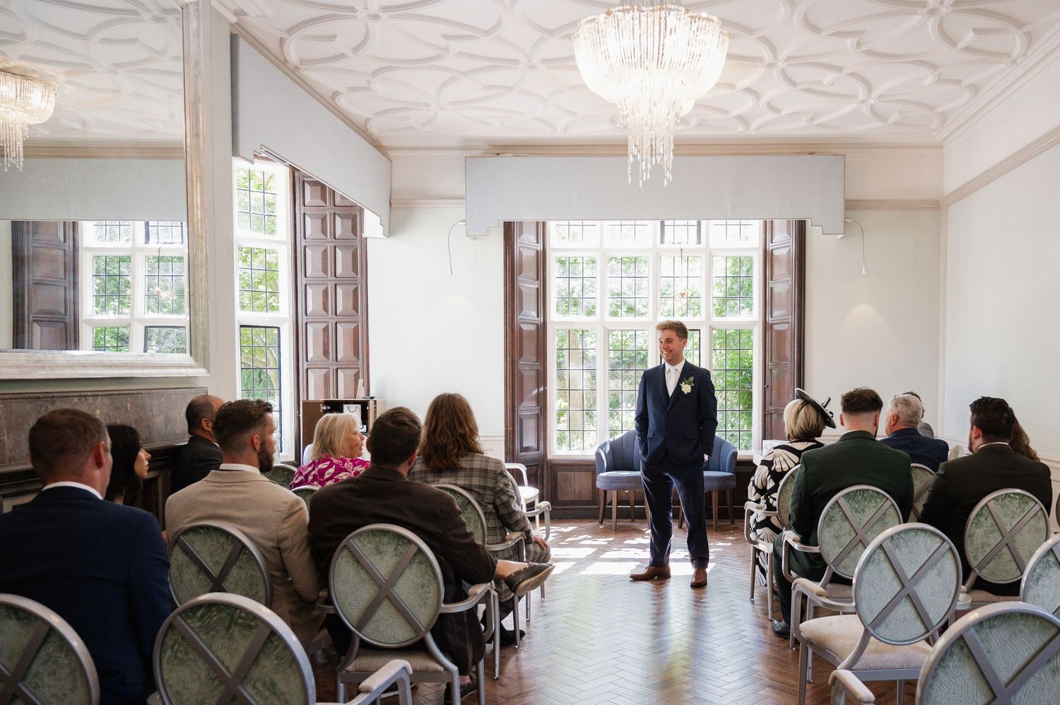 Groom stands at the altar in an elegant chandelier-lit ceremony room as wedding guests await the bride's arrival.