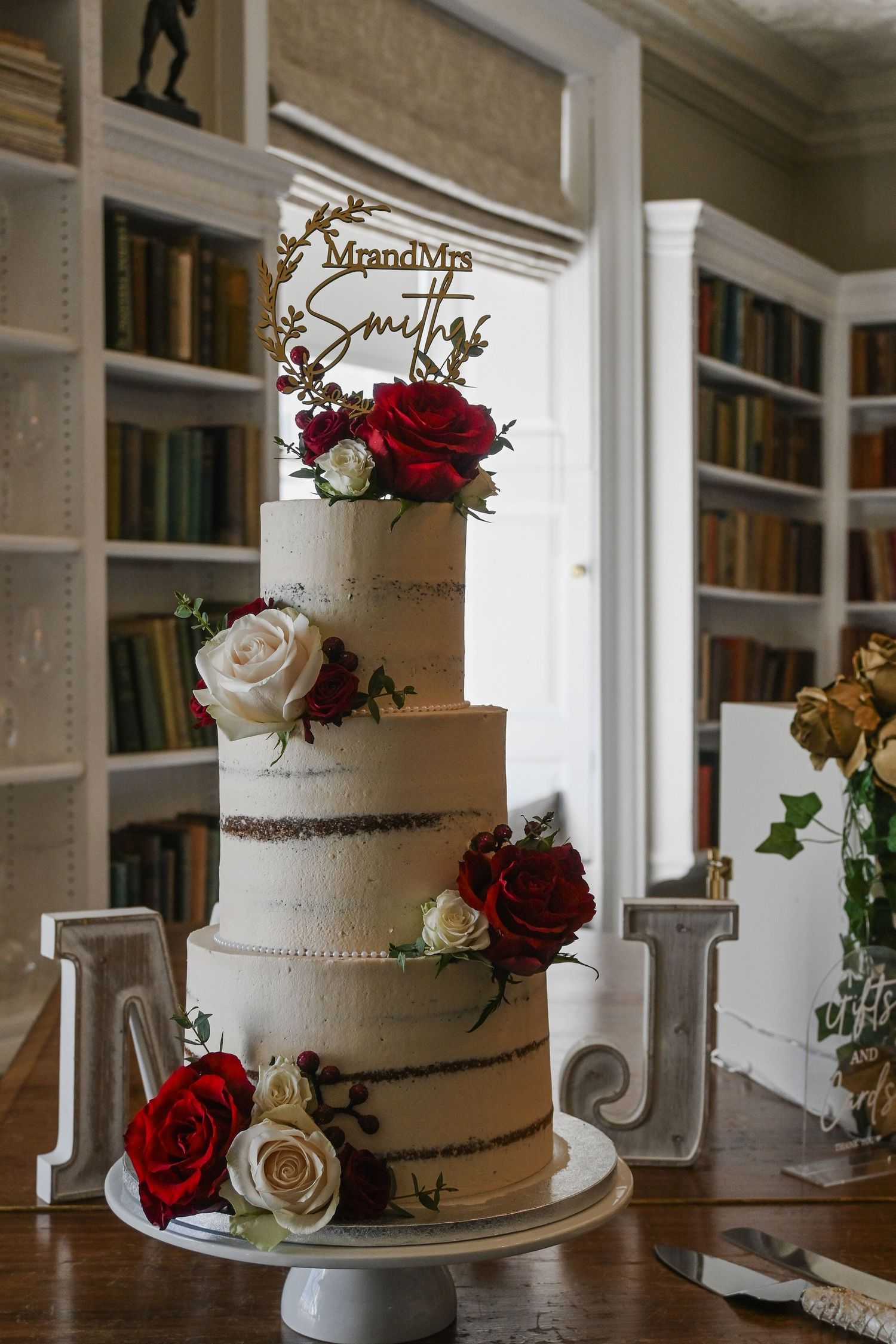 Elegant three-tier semi-naked wedding cake with red and white roses and Mr and Mrs Smith topper.
