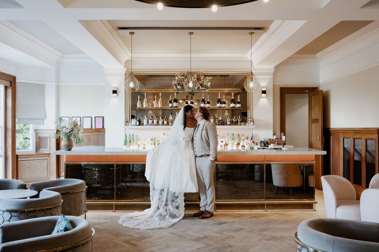 Bride and groom share a romantic moment in front of an elegant bar with chandelier lighting at their wedding venue.